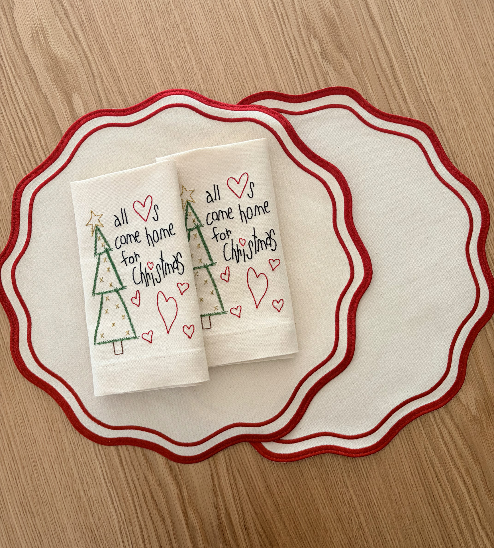 Guardanapos de Natal bordados com textos e corações sobre placemats creme com borda vermelha ondulada
