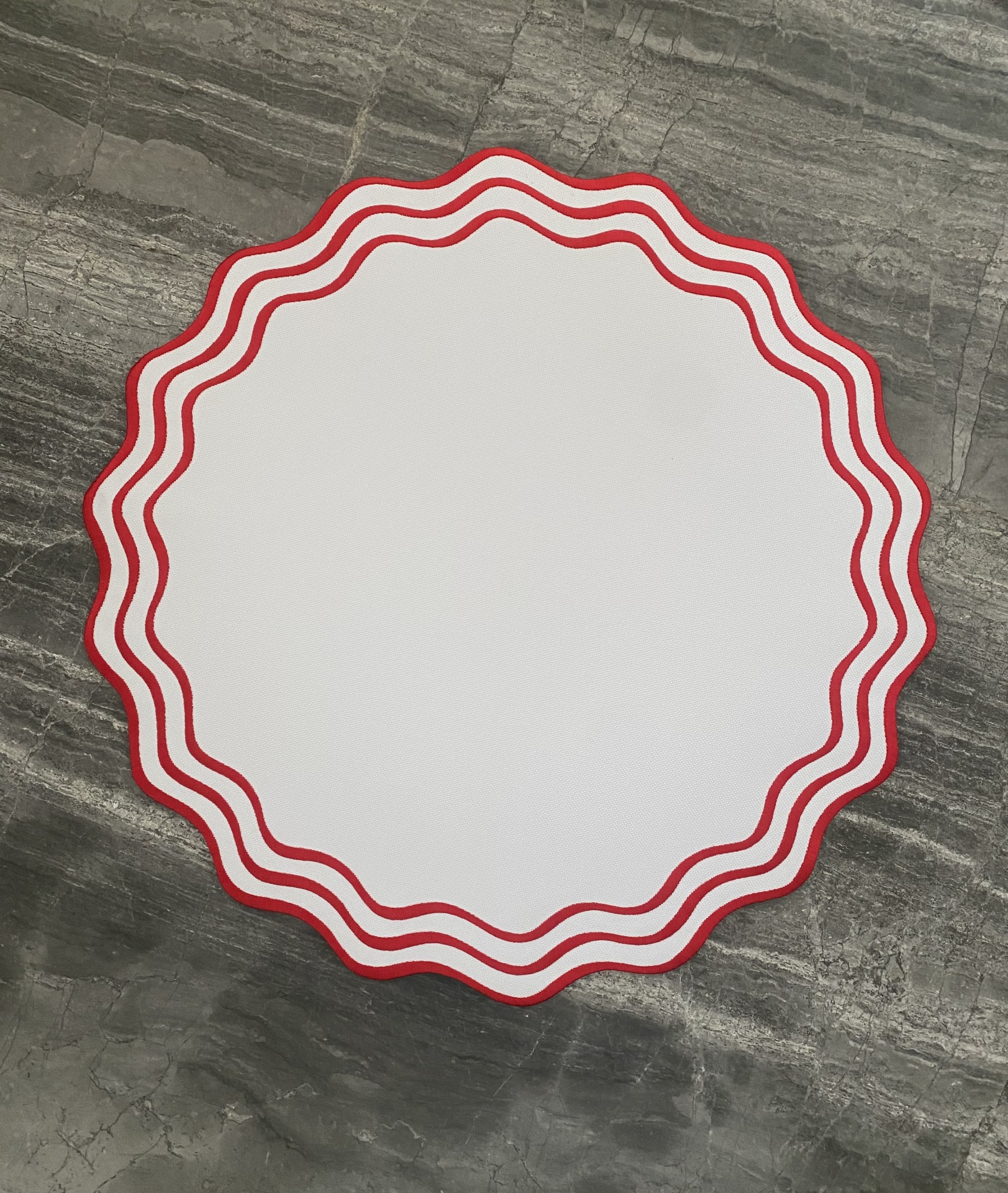 Mesa redonda branca com borda ondulada vermelha sobre chão cinzento