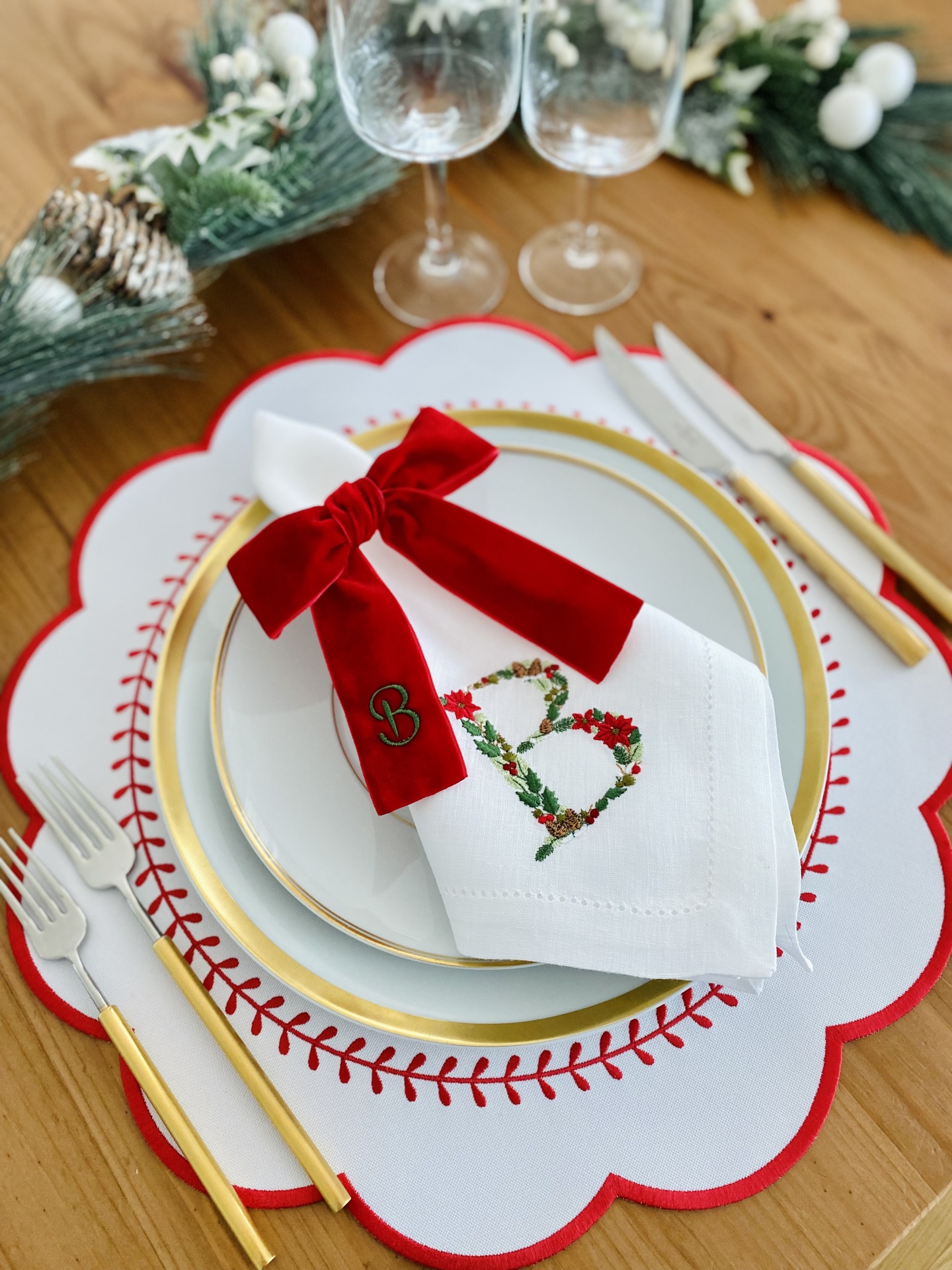 Conjunto de pratos, guardanapo com laço vermelho, talheres dourados e decoração natalícia numa mesa de madeira