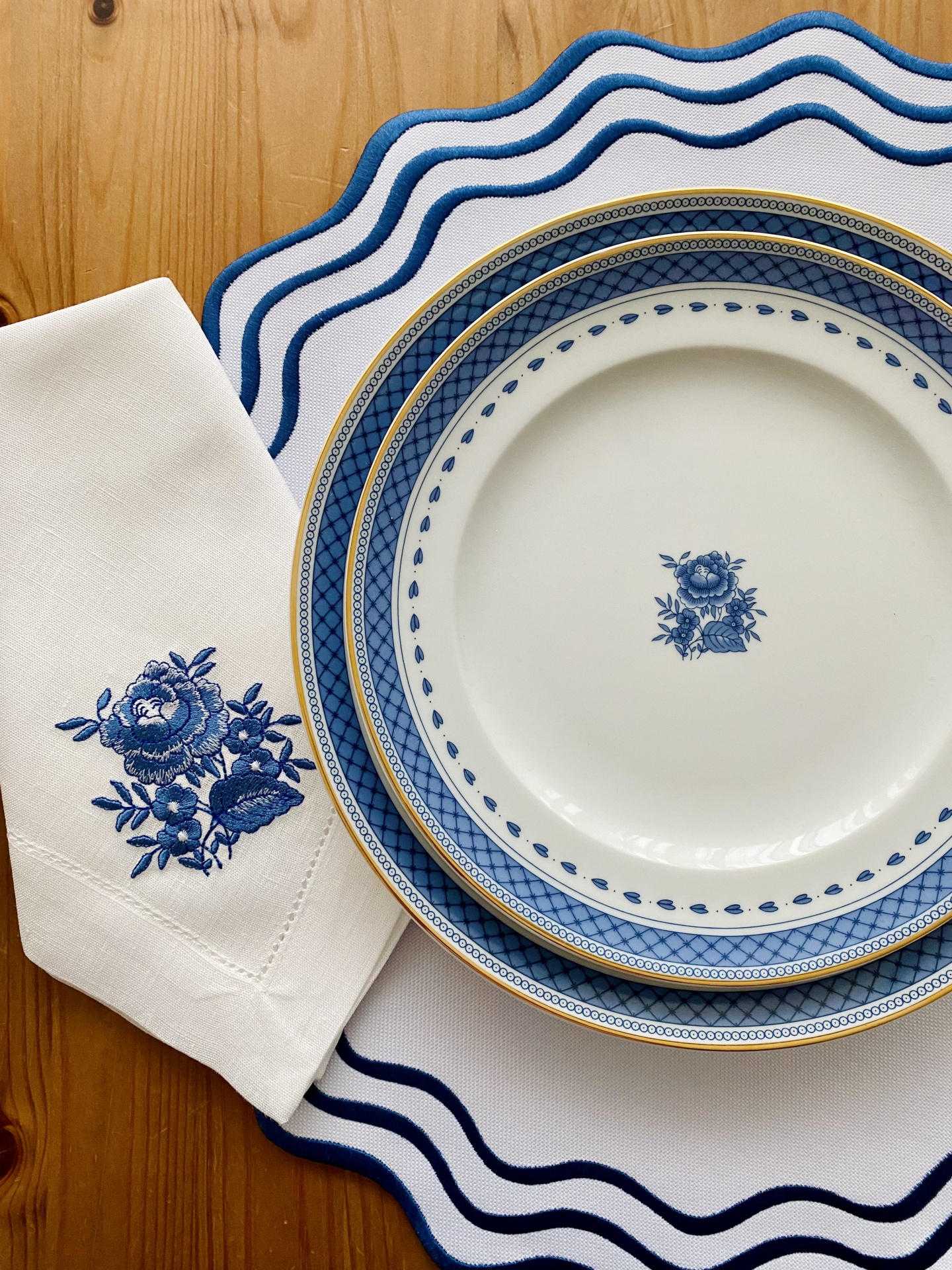 Conjunto de pratos de porcelana azul e dourada com guardanapo bordado e caminho de mesa branco com borda azul