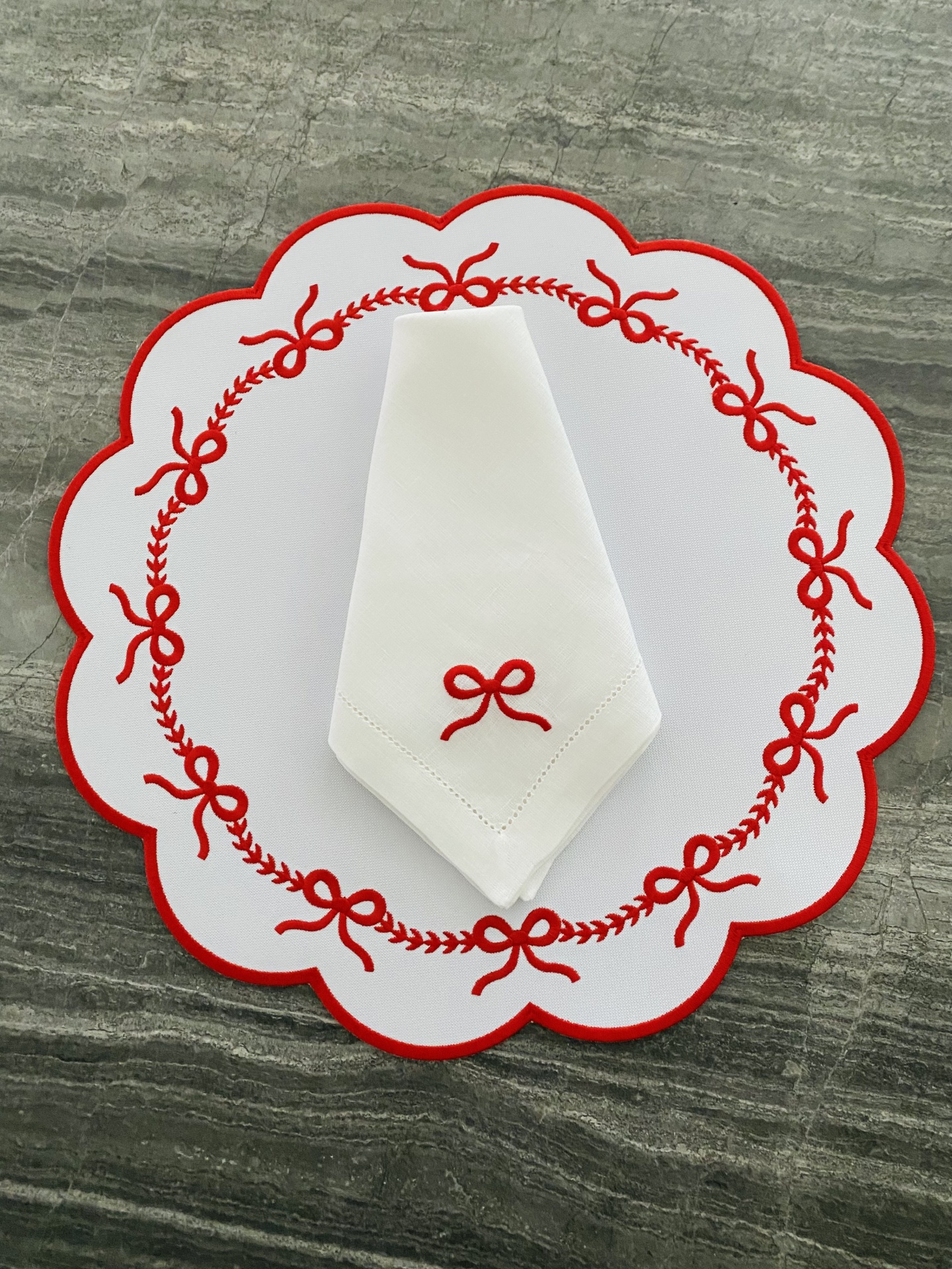 Guardanapo branco bordado com laço vermelho sobre sousplat branco bordado com laços vermelhos