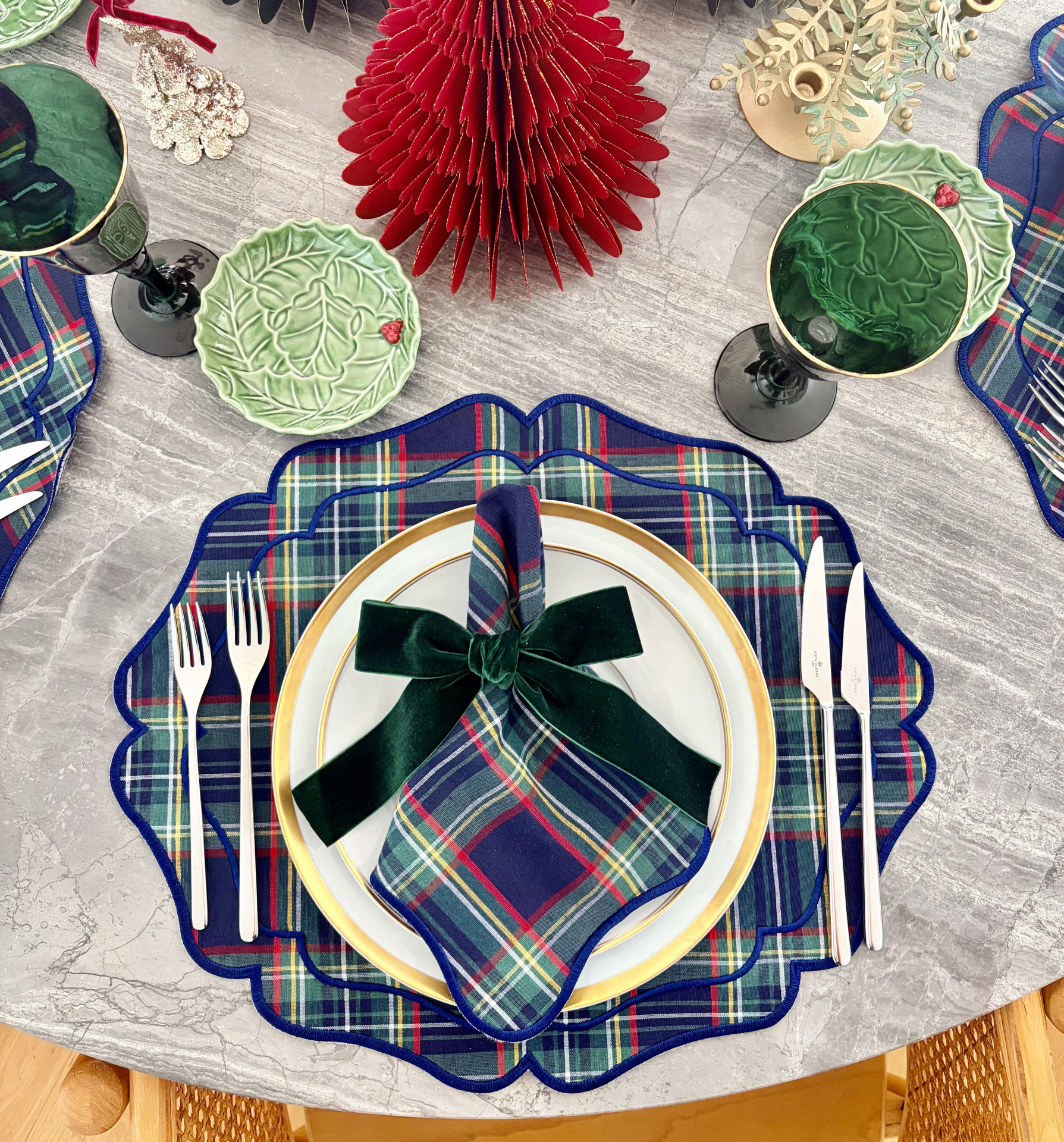 Conjunto de jantar com pratos de porcelana e guardanapos xadrez, copos verdes, talheres de aço, pratos pequenos verdes com relevo, decorados para mesa festiva.