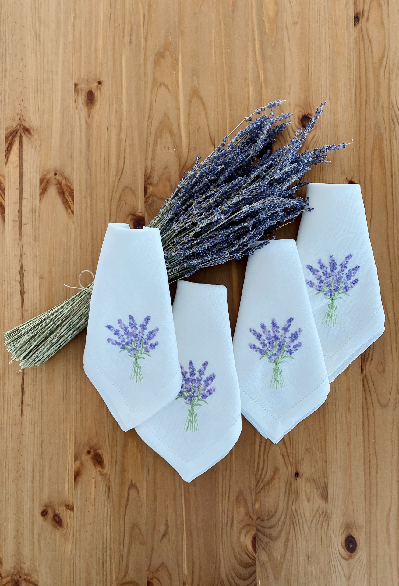 Guardanapos brancos com bordados de lavanda e feixe de lavanda seca numa mesa de madeira