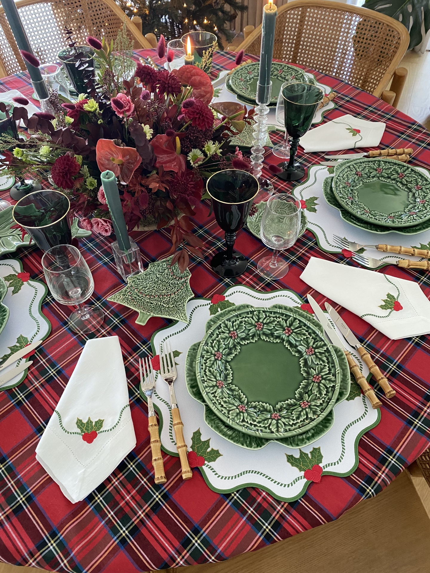 Mesa de jantar decorada para Natal com pratos verdes, toalha tartan vermelha e guardanapos bordados.