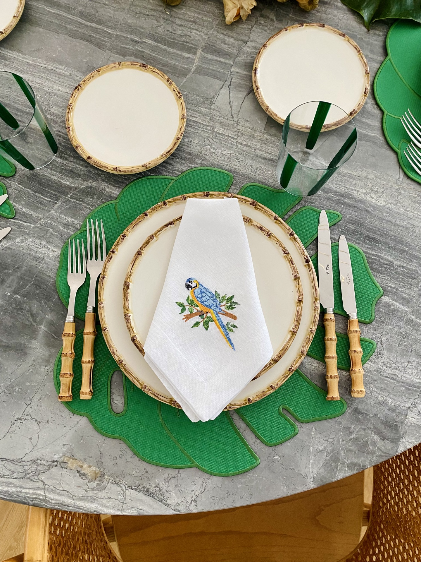 Mesa posta com louça e talheres com tema bambu e guardanapo com papagaio bordado