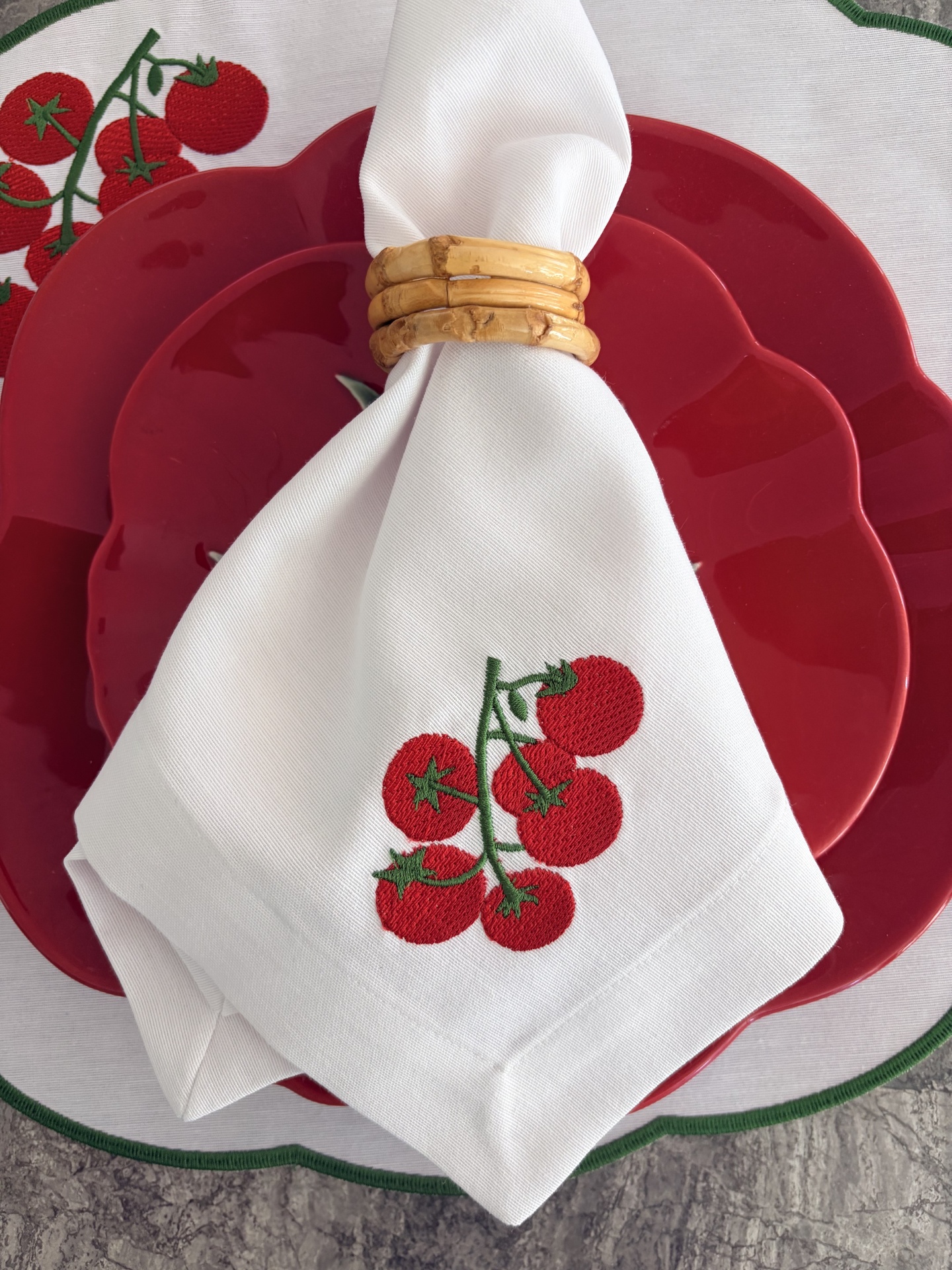 Pratos vermelhos com guardanapo branco bordado com tomates e porta-guardanapo de madeira
