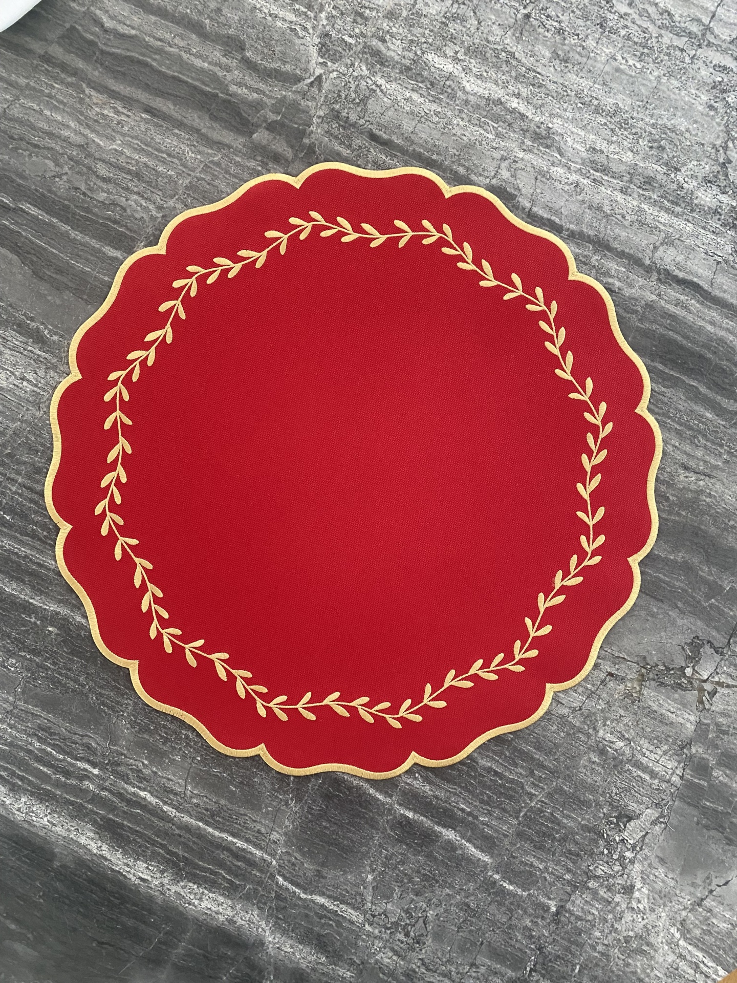 Toalha de mesa vermelha redonda com bordas onduladas e bordado dourado colocada sobre pedra cinzenta