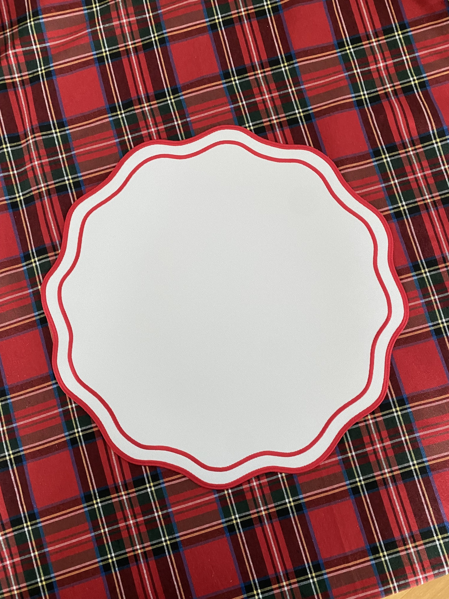 Base para bolo ou prato redonda de papel branco com borda vermelha sobre superfície xadrez.