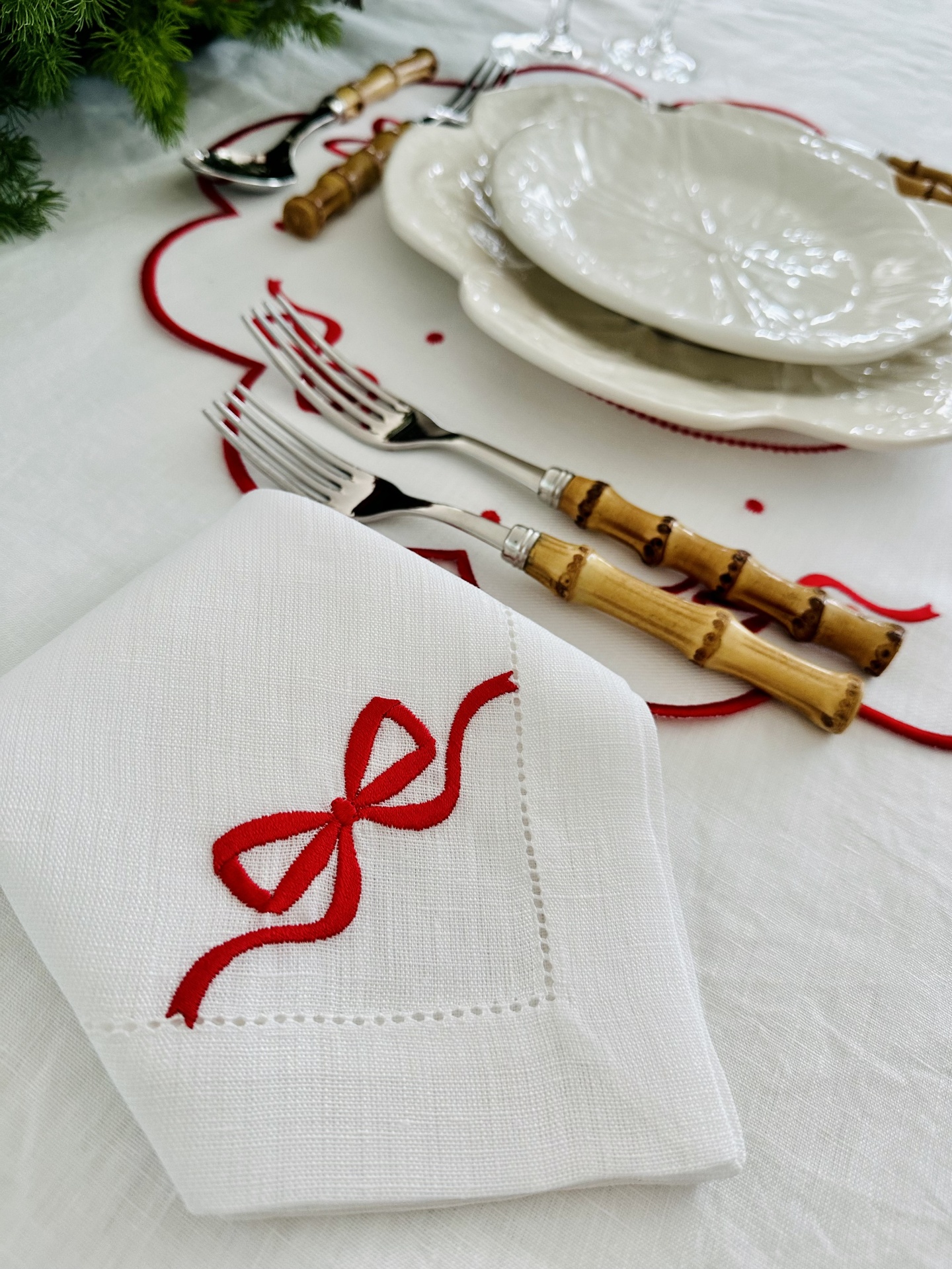 Conjunto de talheres de madeira, pratos brancos com relevo, guardanapo com bordado vermelho