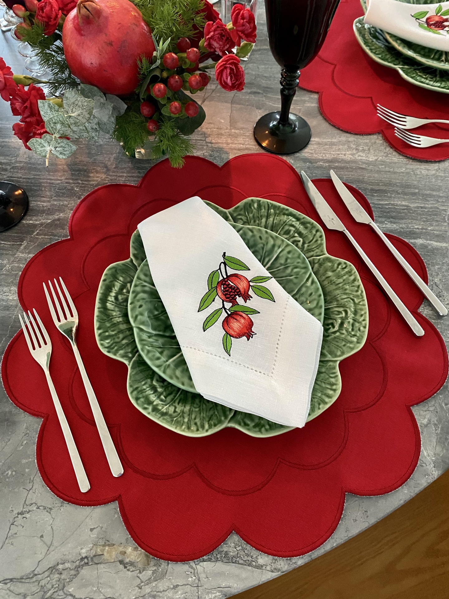 Conjunto de loiça verde com pratos em forma de folha, guardanapo bordado, jogos americanos vermelhos ondulados, talheres prateados e copo preto