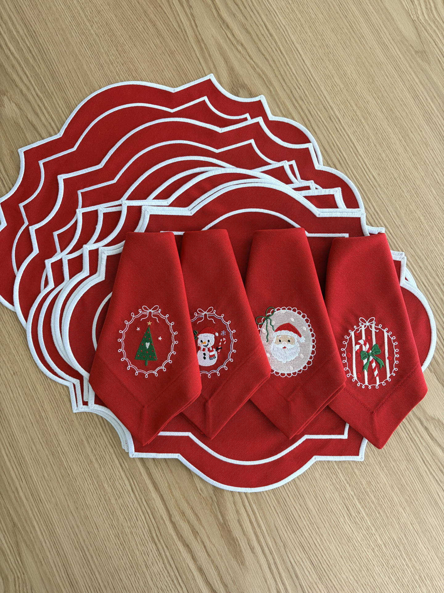 Jogos americanos e guardanapos vermelhos com bordados de Natal em mesa de madeira clara.