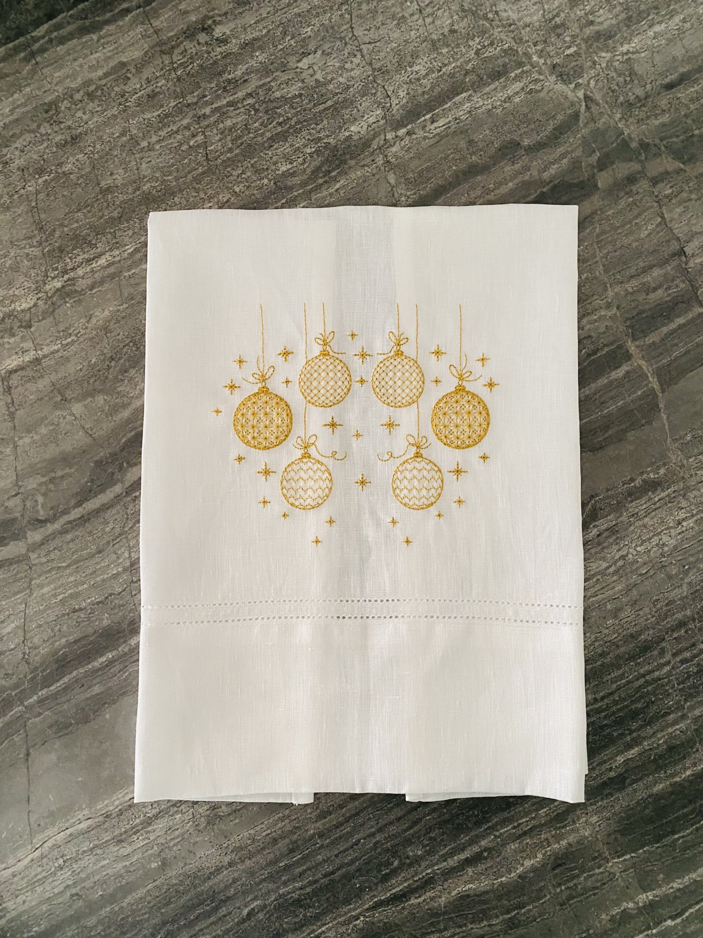 Toalha branca com bordado dourado de bolas de Natal em superfície cinzenta
