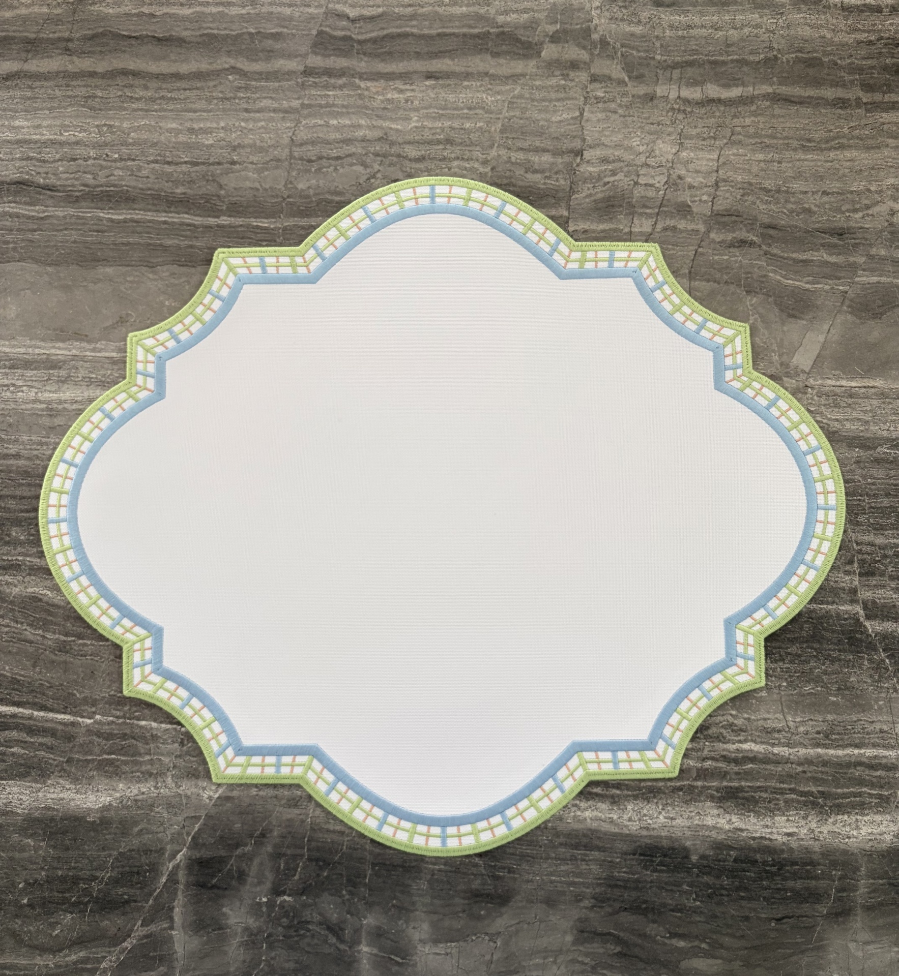 Jogo americano branco com borda quadriculada azul e verde sobre pedra cinzenta