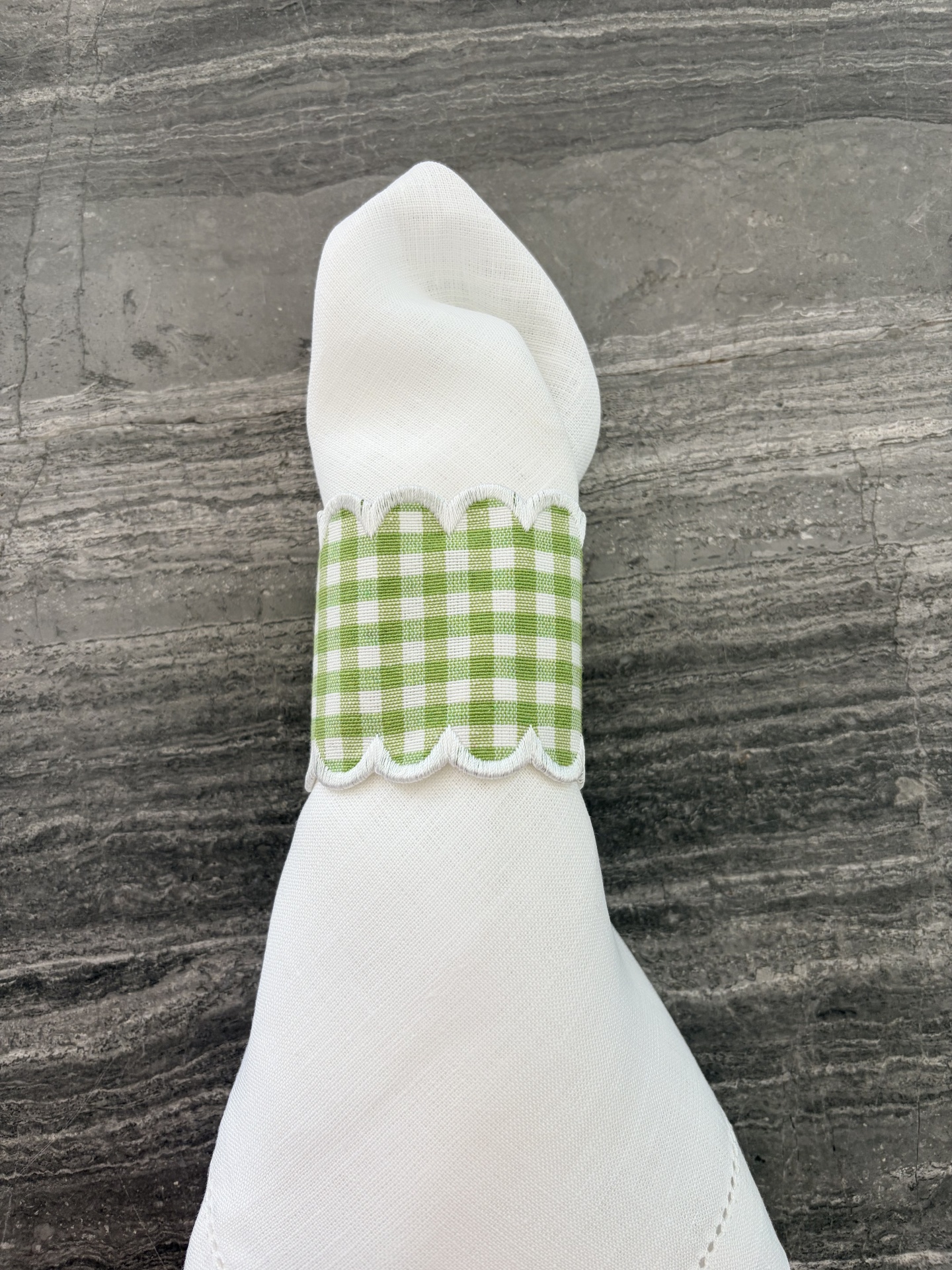 Guardanapo branco com argola verde quadriculada em superfície cinza