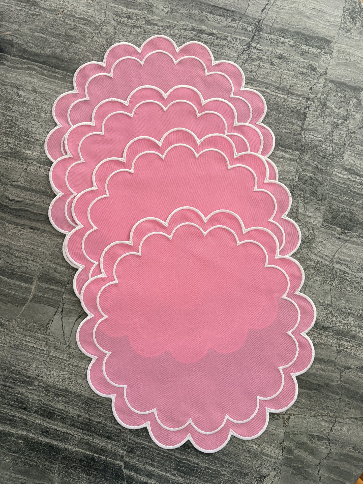 Individuais de mesa cor-de-rosa com borda branca ondulada em superfície de pedra cinza.