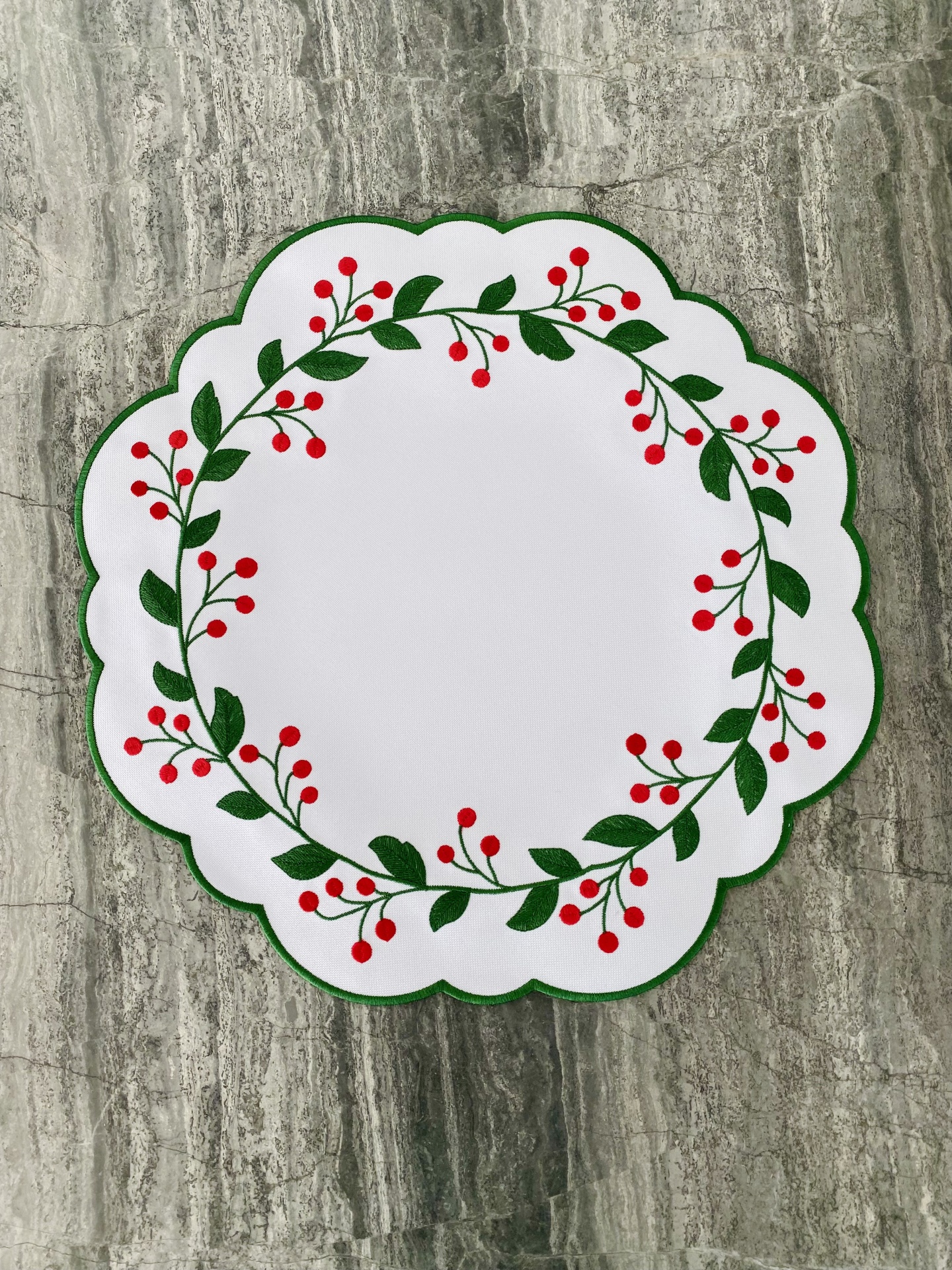 Guardanapo branco com borda verde e padrão de folhas verdes e bagas vermelhas.