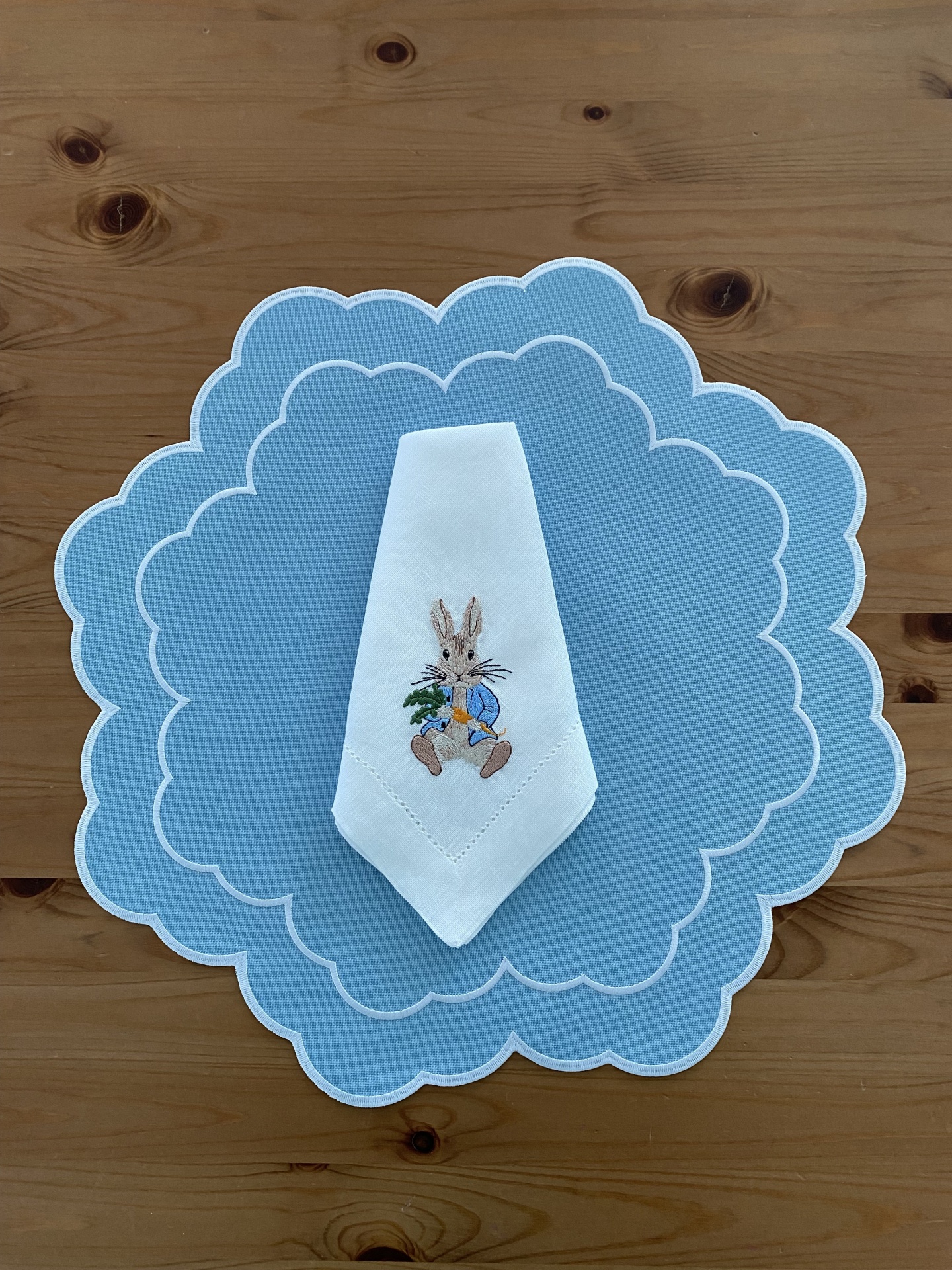 Toalha azul clara com borda branca e guardanapo branco com bordado de coelho