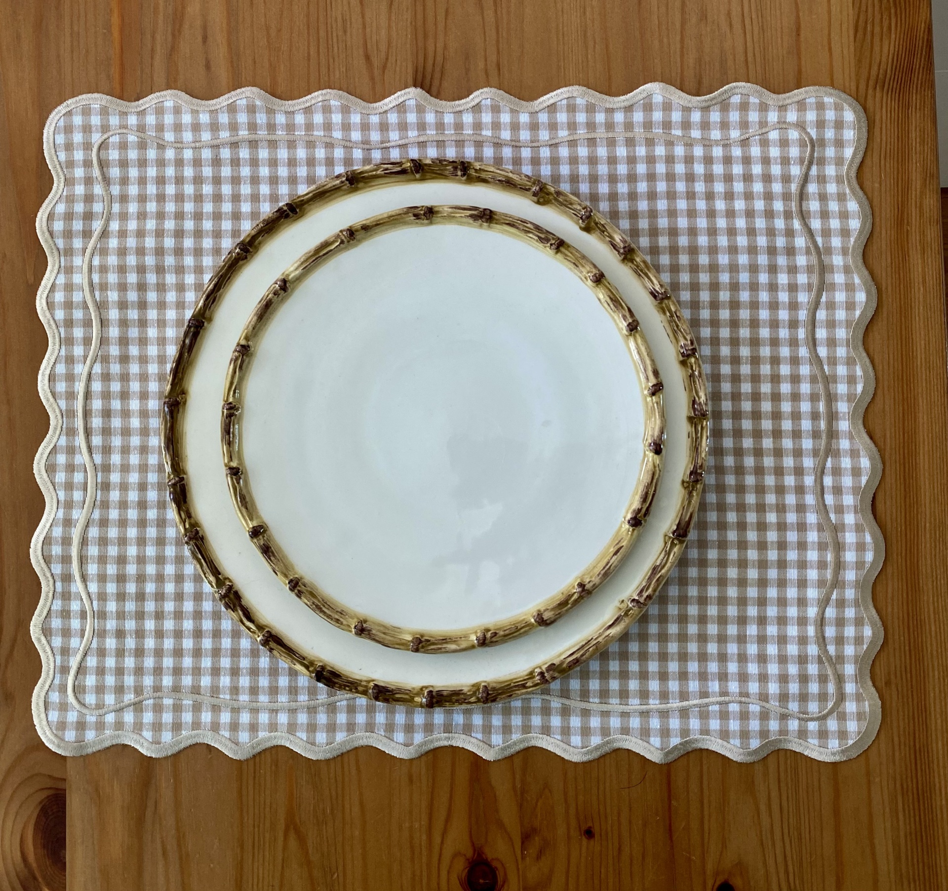 dois pratos brancos com bordas de padrão de ramos sobre base xadrez bege e branca com bordas onduladas