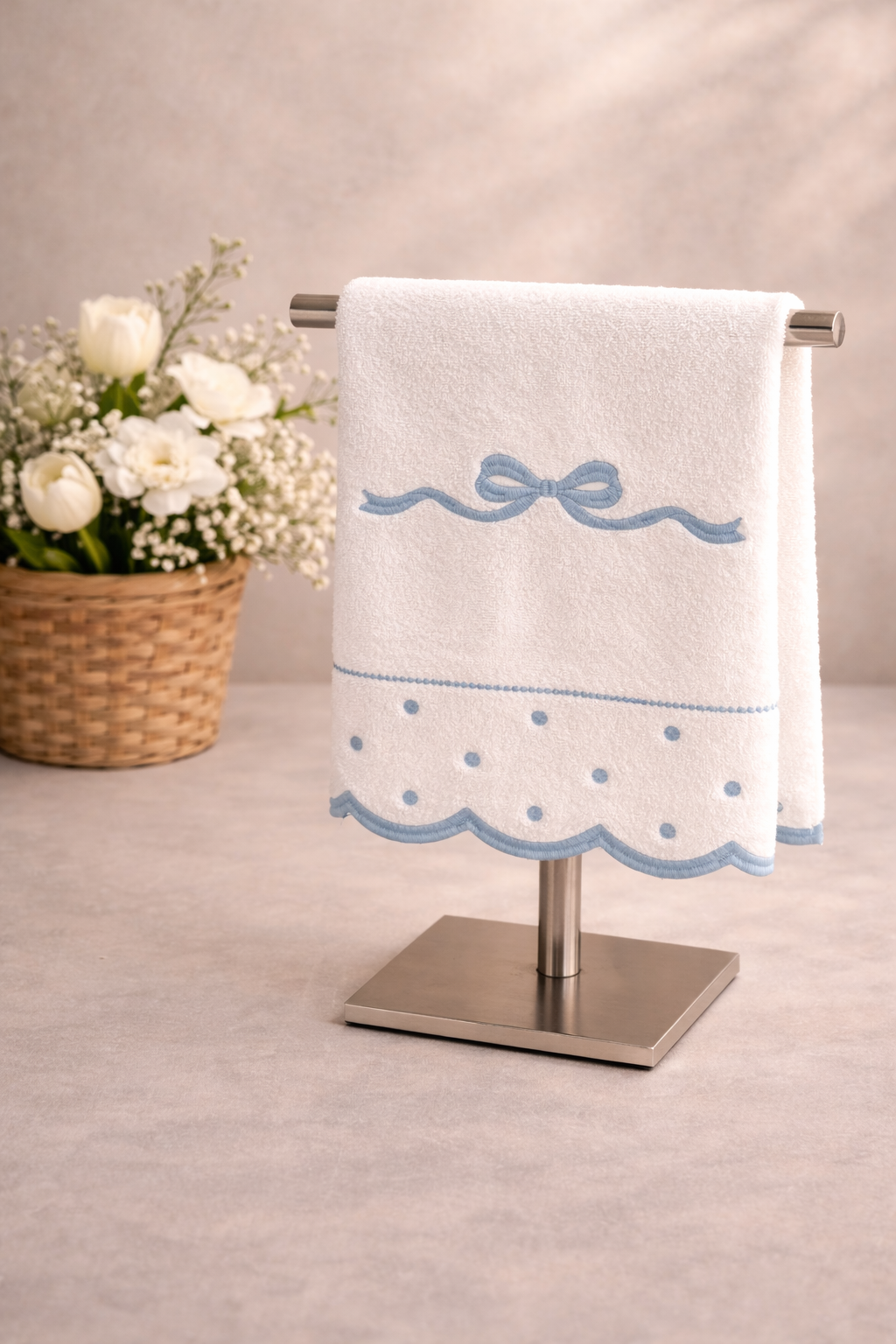 Toalha branca com bordado azul pendurada em suporte metálico e cesto de flores ao lado