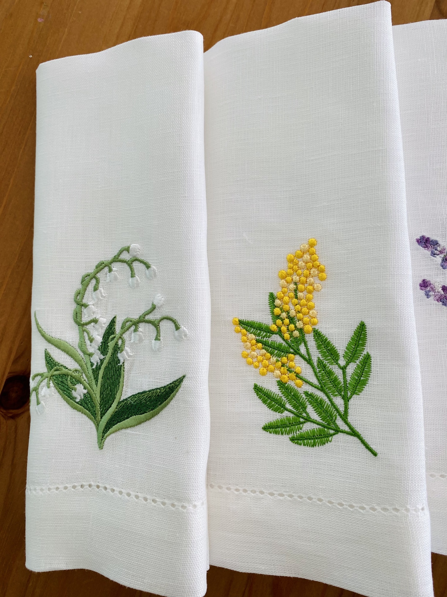 Três guardanapos brancos com bordados florais coloridos