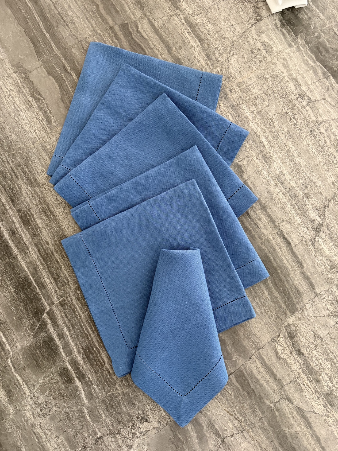 Guardanapos de tecido azul com borda decorativa sobre mesa de pedra cinzenta