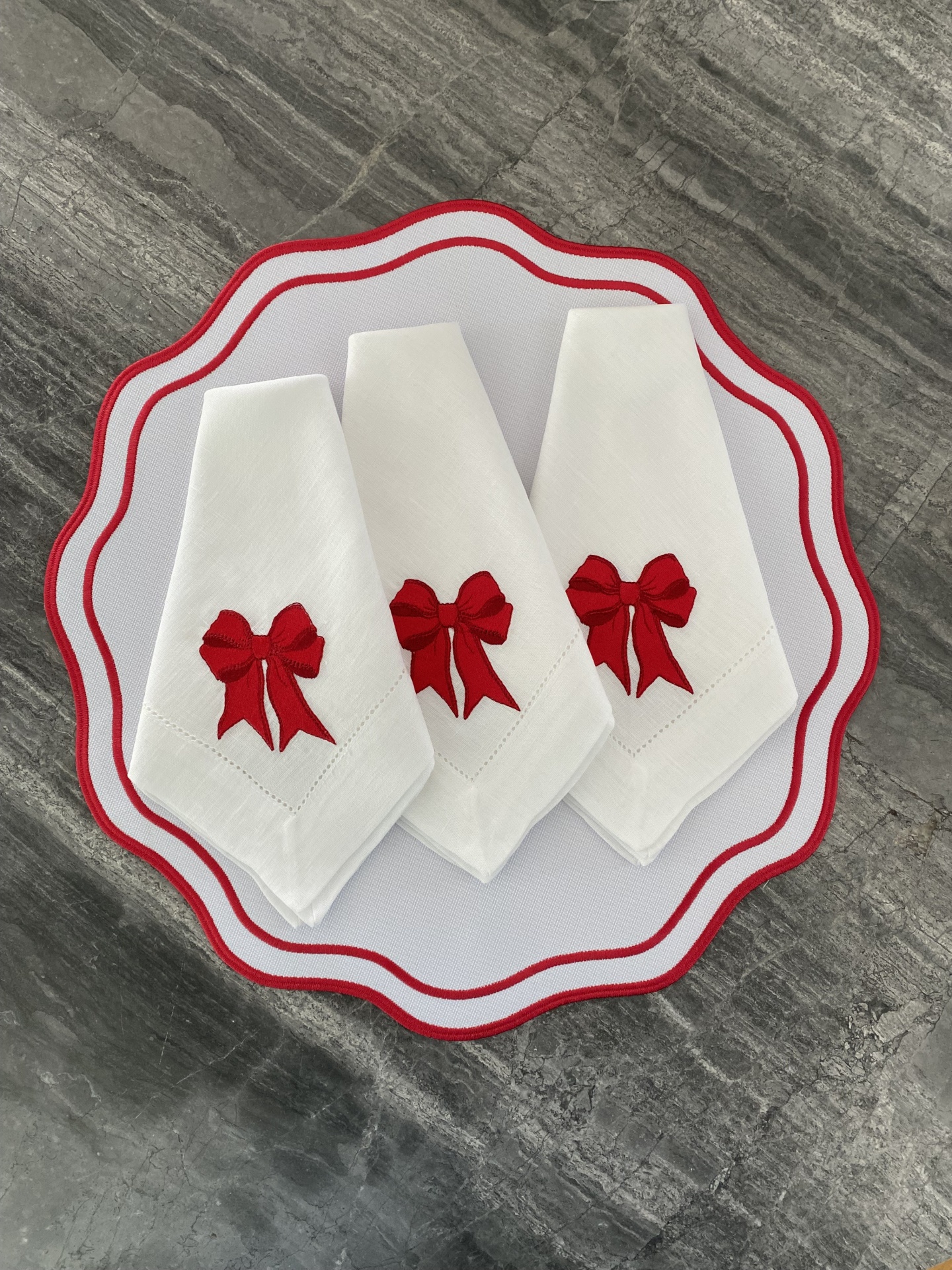 Três guardanapos brancos com laços vermelhos sobre base branca com borda vermelha