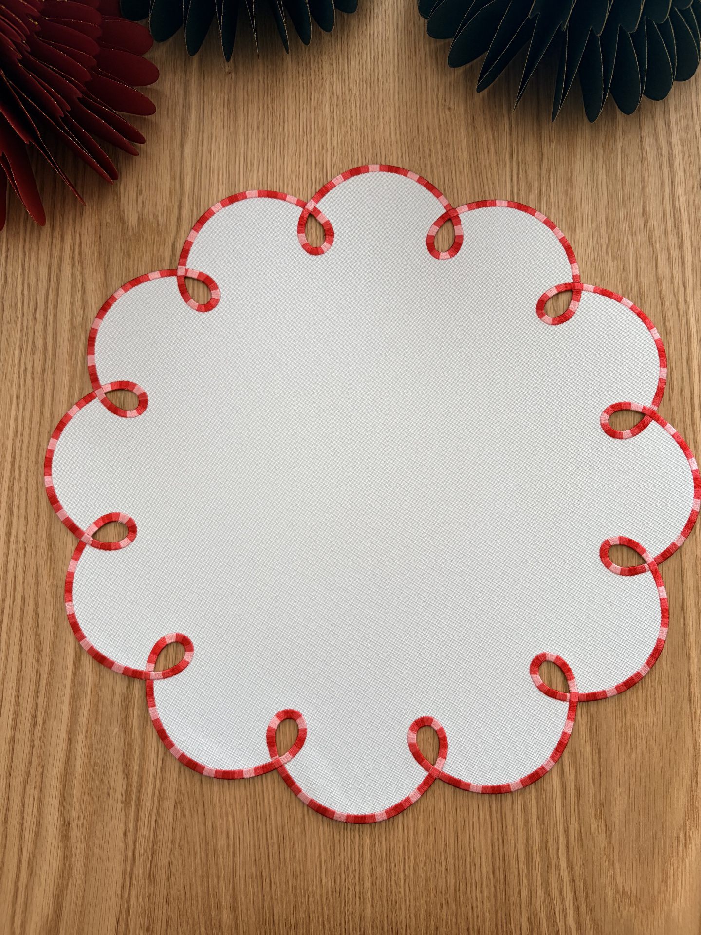 Toalha redonda branca com bordas onduladas em tecido vermelho e branco sobre mesa de madeira