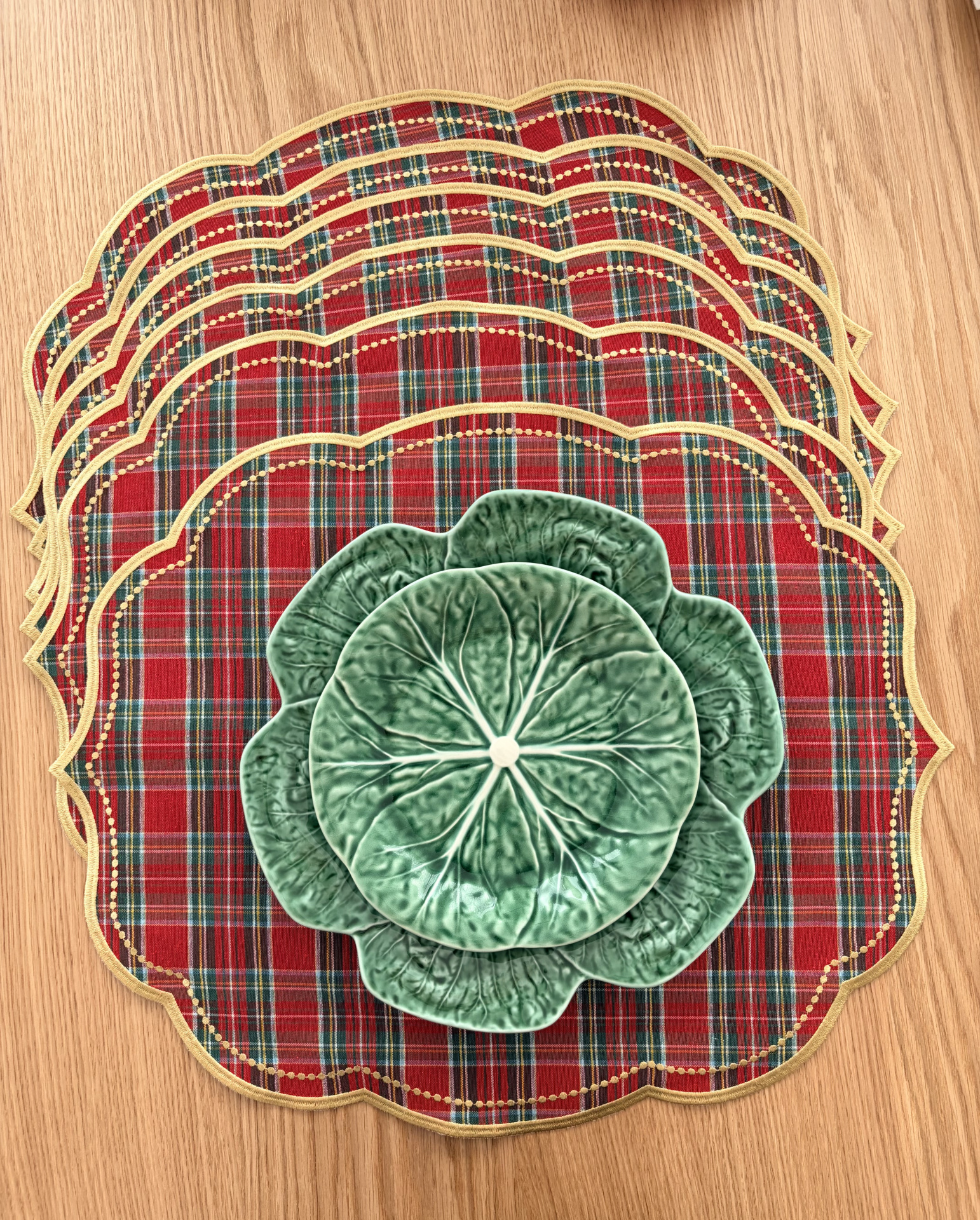 Bases de prato tartan e pratos decorativos verdes com forma de folhas sobre mesa de madeira.