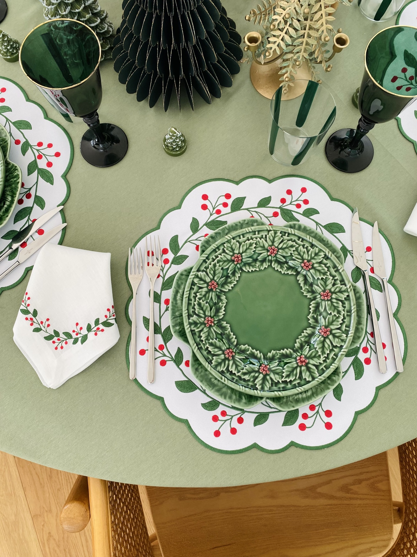 Jantar de Natal com pratos e copos decorativos em verde e vermelho sobre mesa com toalha verde claro