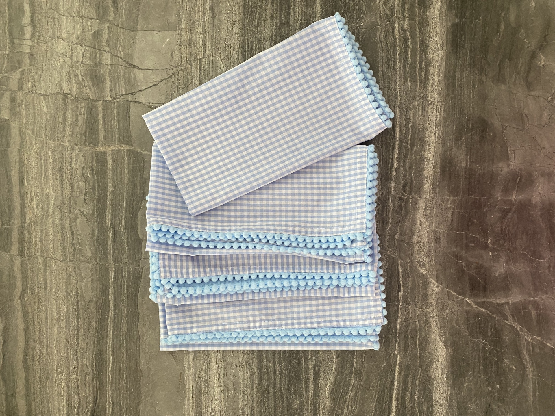 Paninhos xadrez branco e azul com bordado azul sobre mesa de madeira escura