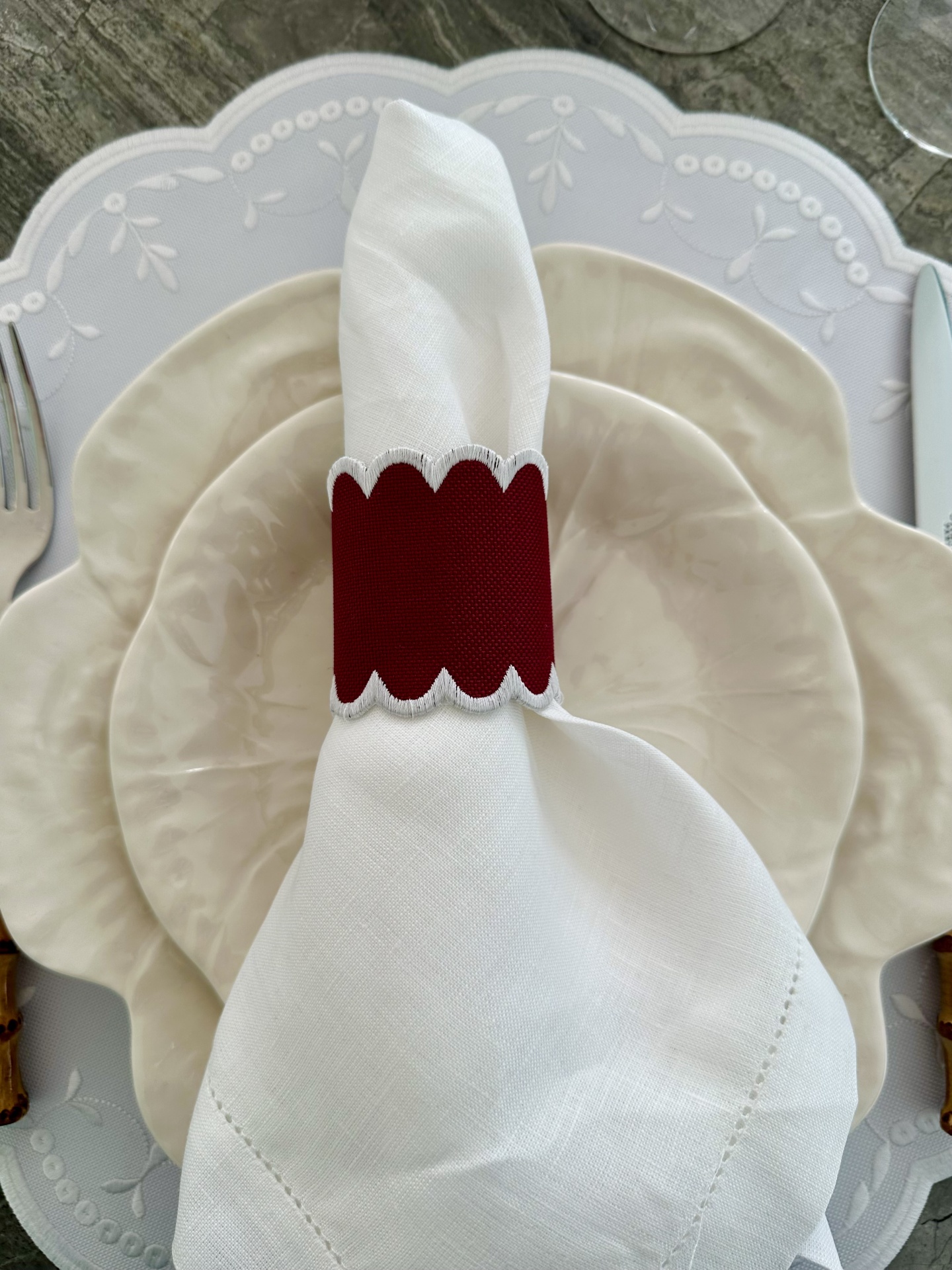 Guardanapo branco com anel de guardanapo vermelho e pratos bege.