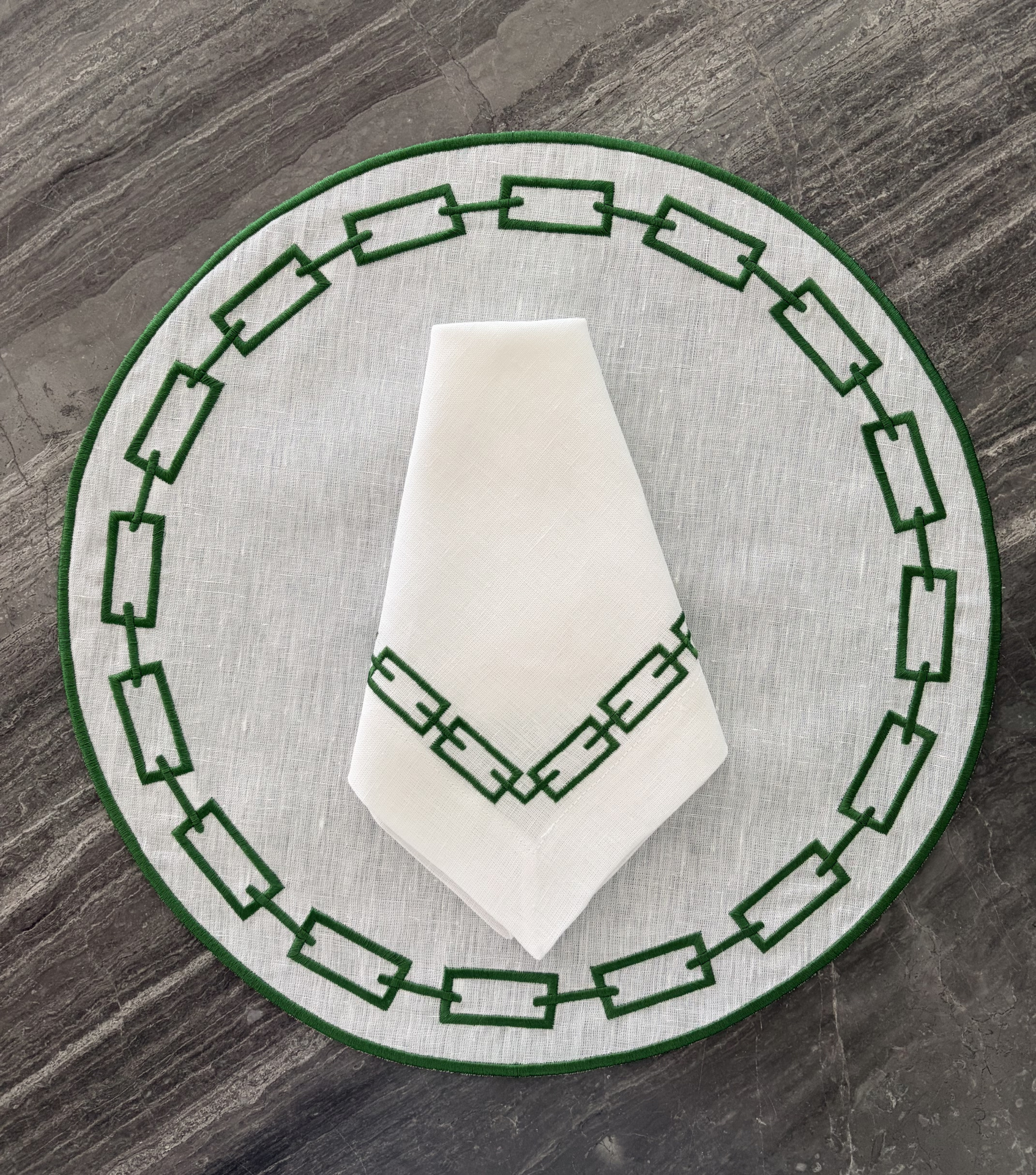 Jogo americano e guardanapo branco com bordado verde geométrico.