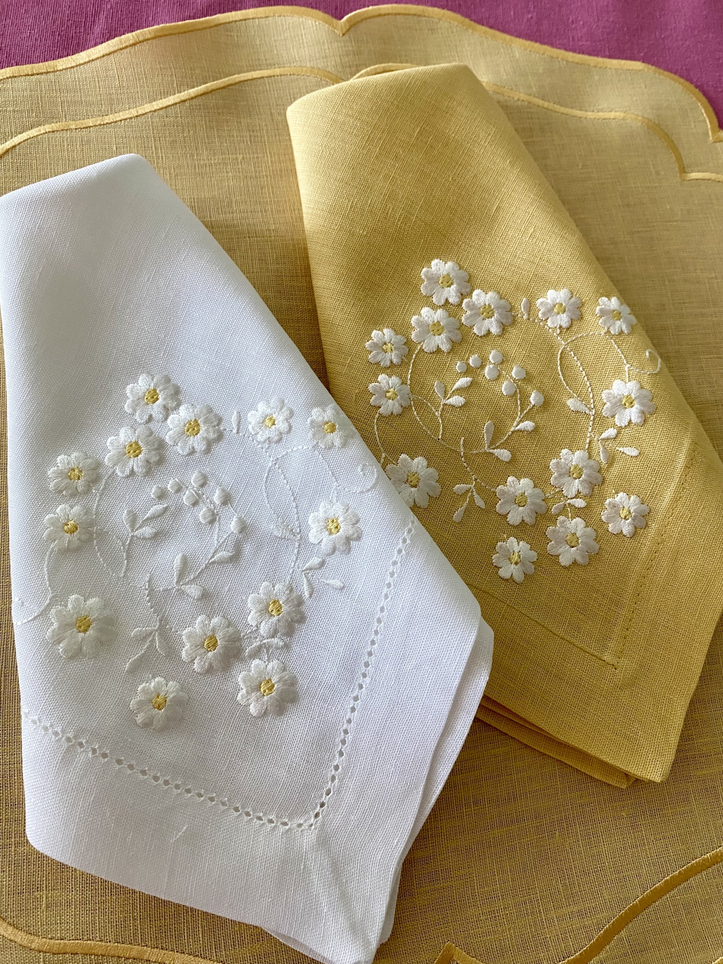 Dois panos de chá bordados, um branco e outro amarelo, com motivos florais, sobre pano amarelo com detalhes dourados