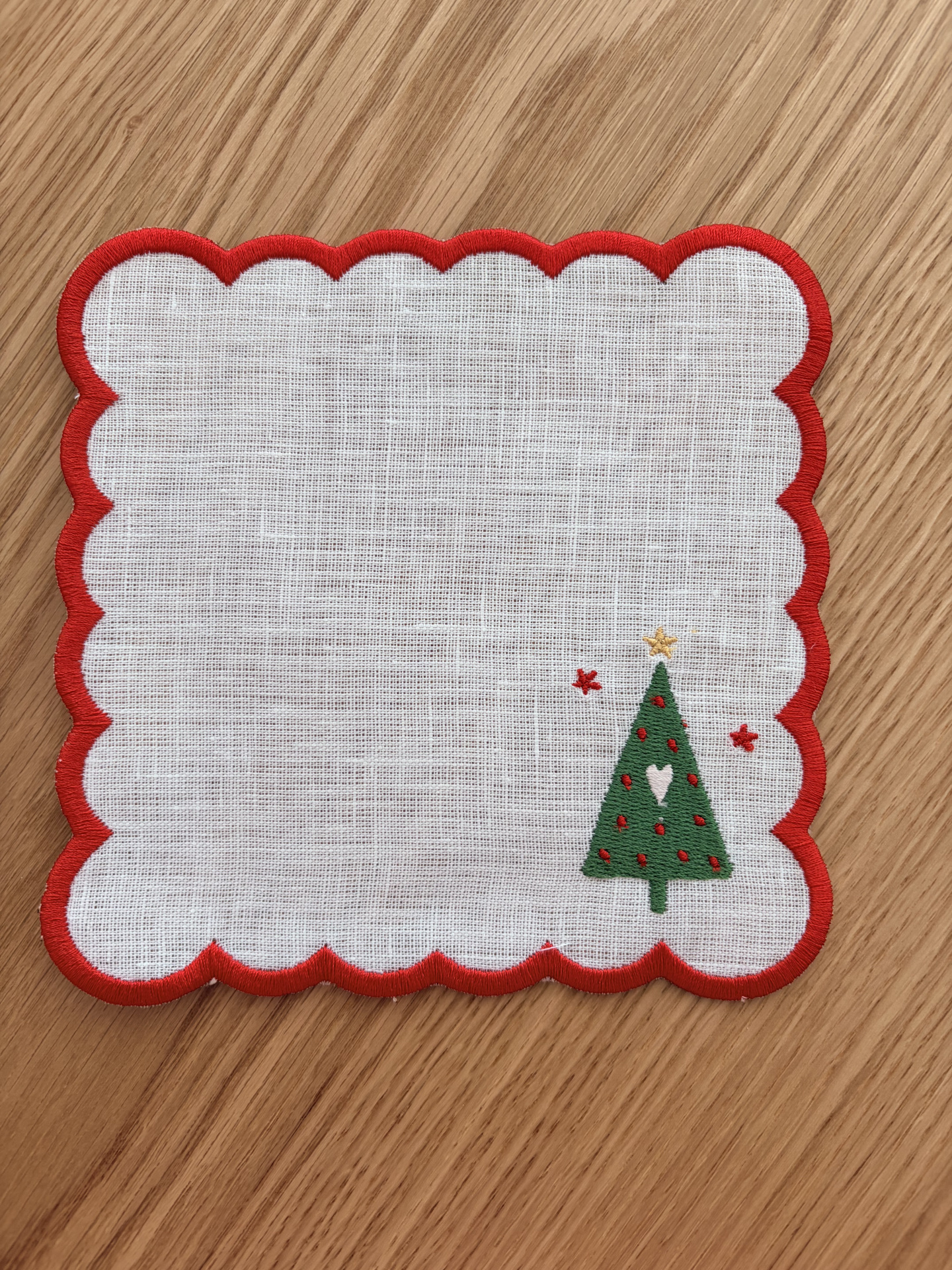 Pano branco com borda vermelha ondulada e bordado de árvore de Natal verde.