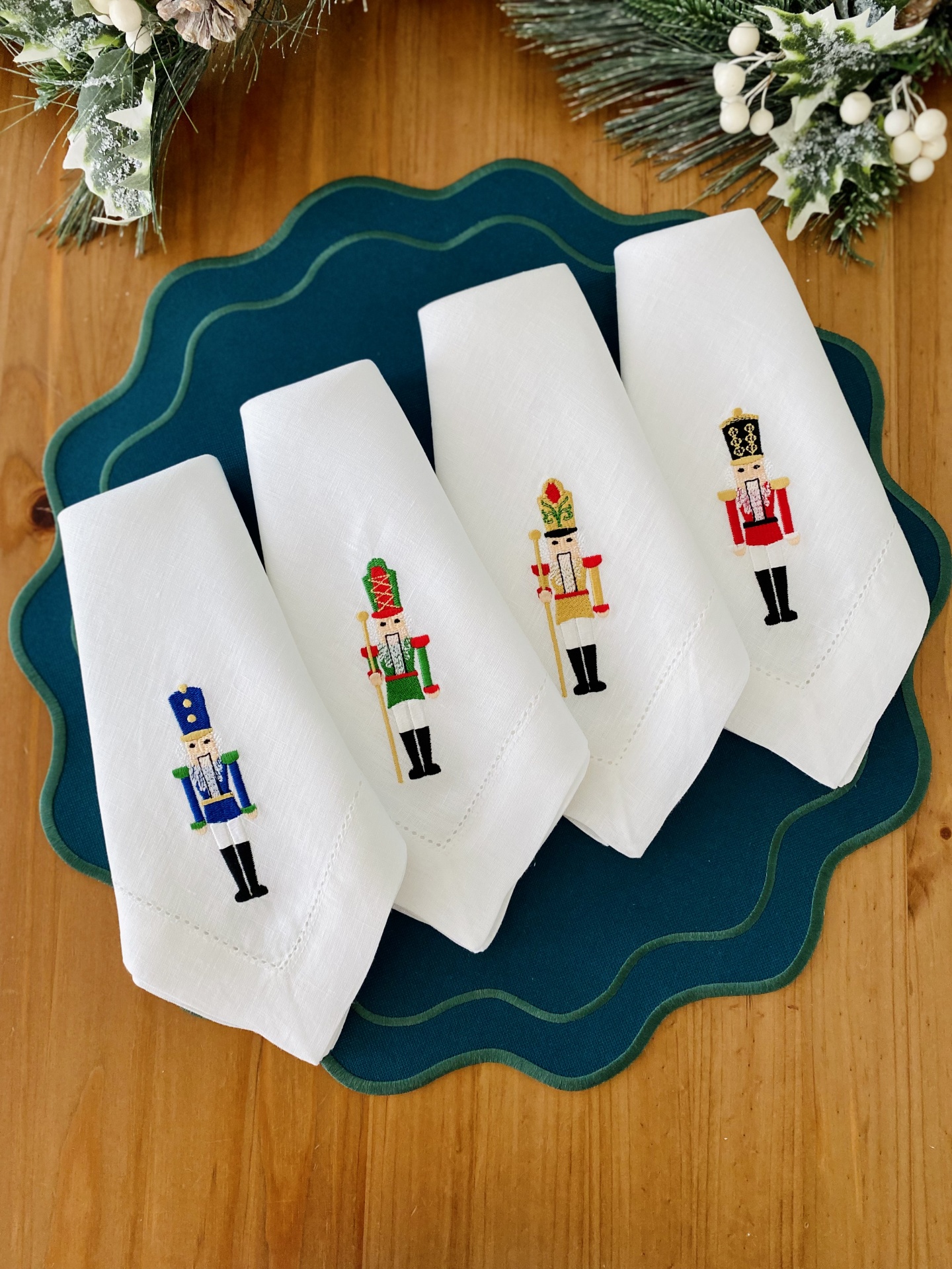 Quatro guardanapos brancos bordados com soldados quebra-nozes sobre apoio de mesa azul escuro e decoração natalícia