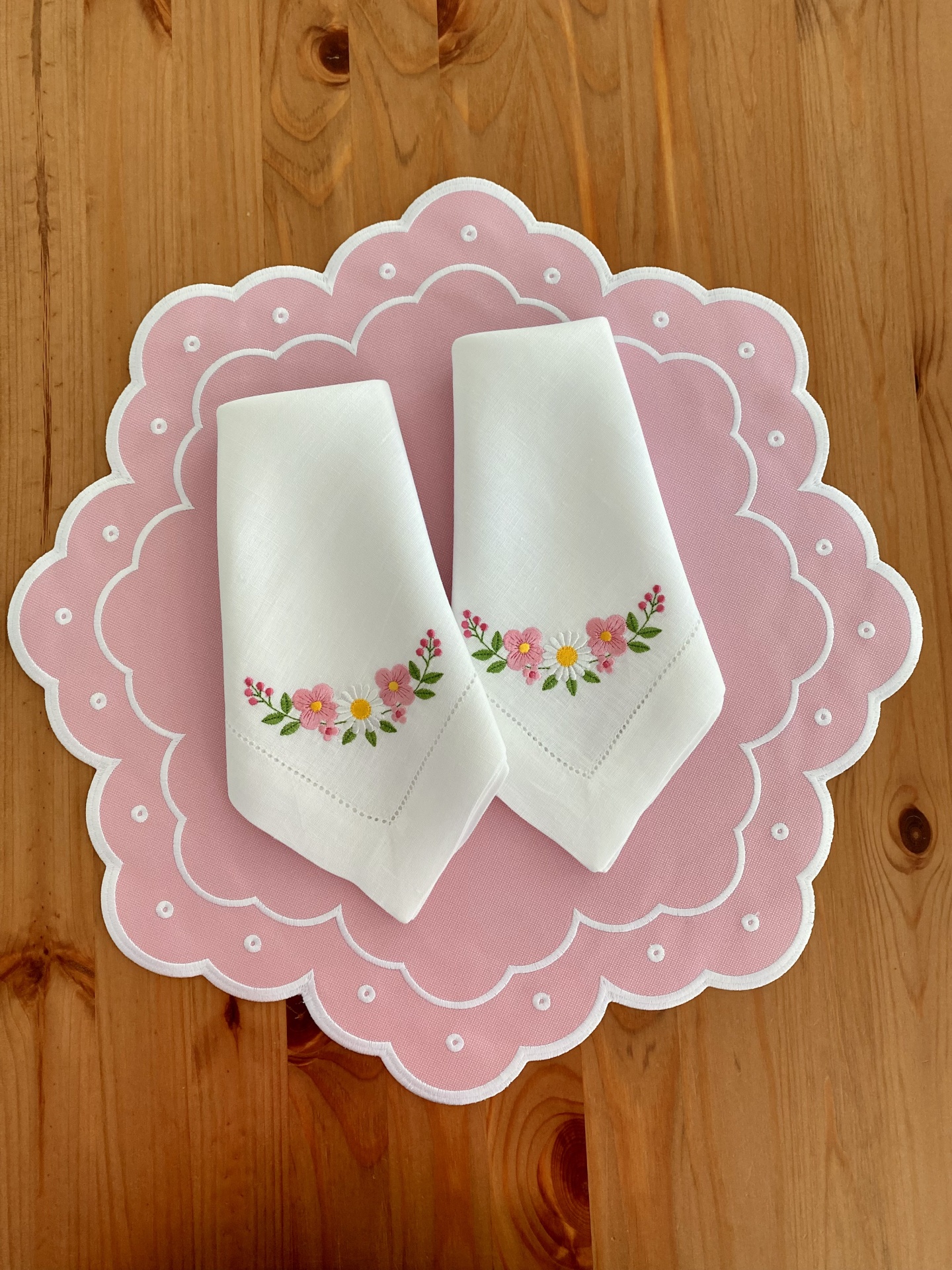 Toalhetes bordados florais sobre apoio rosa em mesa de madeira