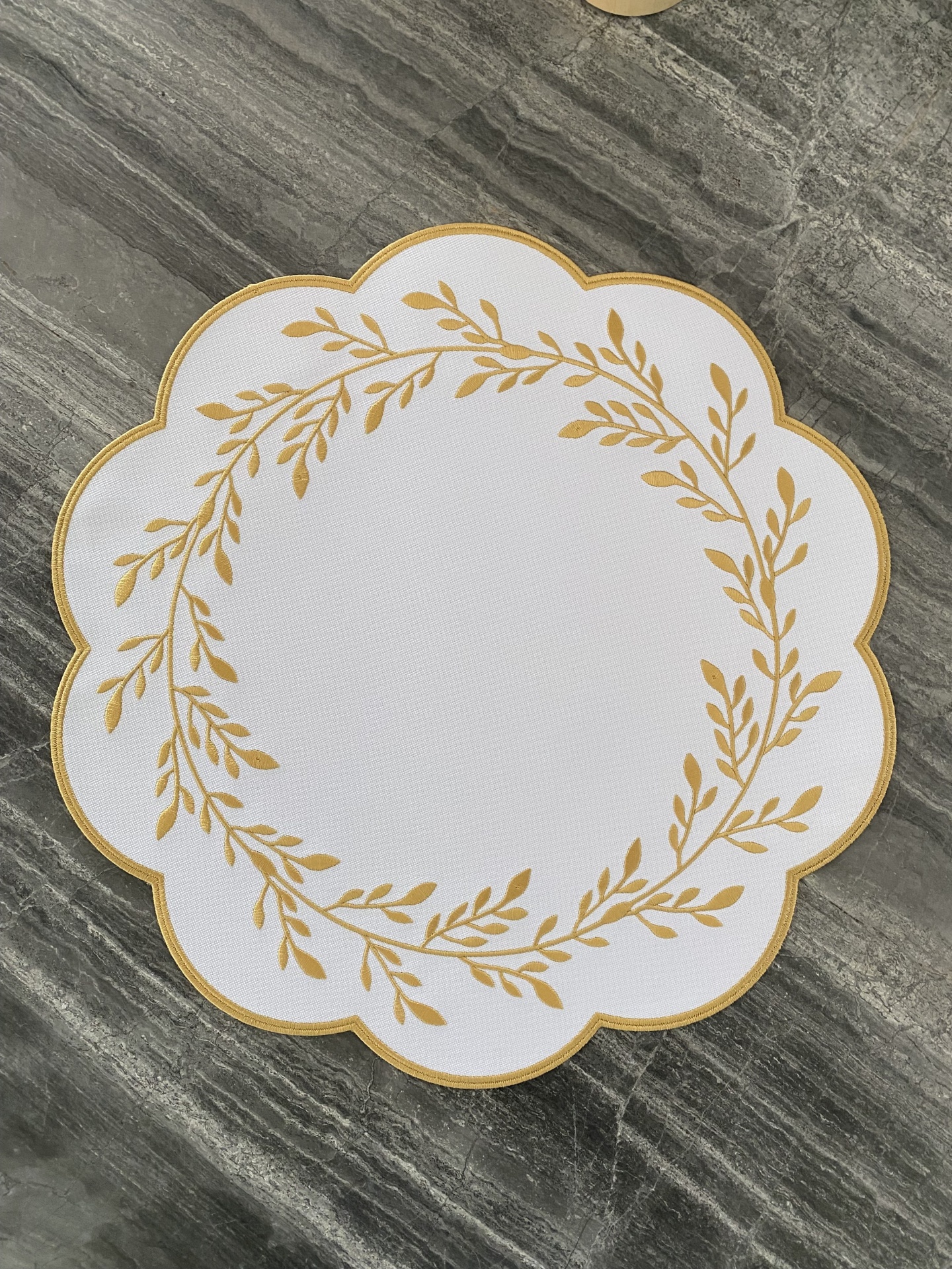 Colher de mesa branca com padrão dourado sobre superfície de pedra cinzenta