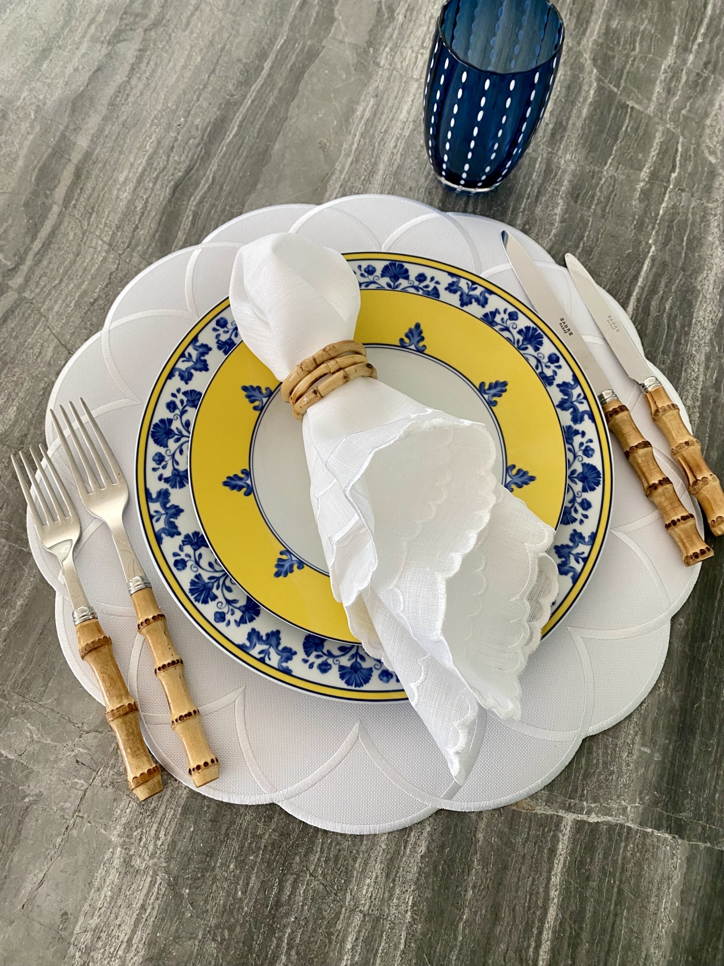 Conjunto de pratos, guardanapo, talheres e copo sobre mesa cinza marmoreada