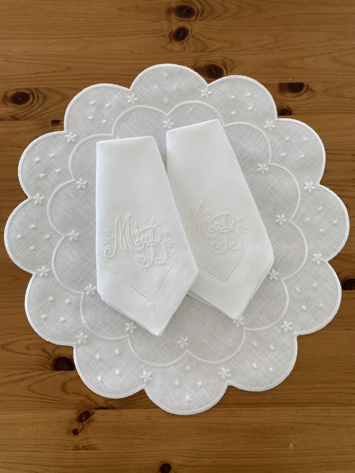 Toalhetes brancos bordados sobre toalhete redondo decorativo branco numa mesa de madeira