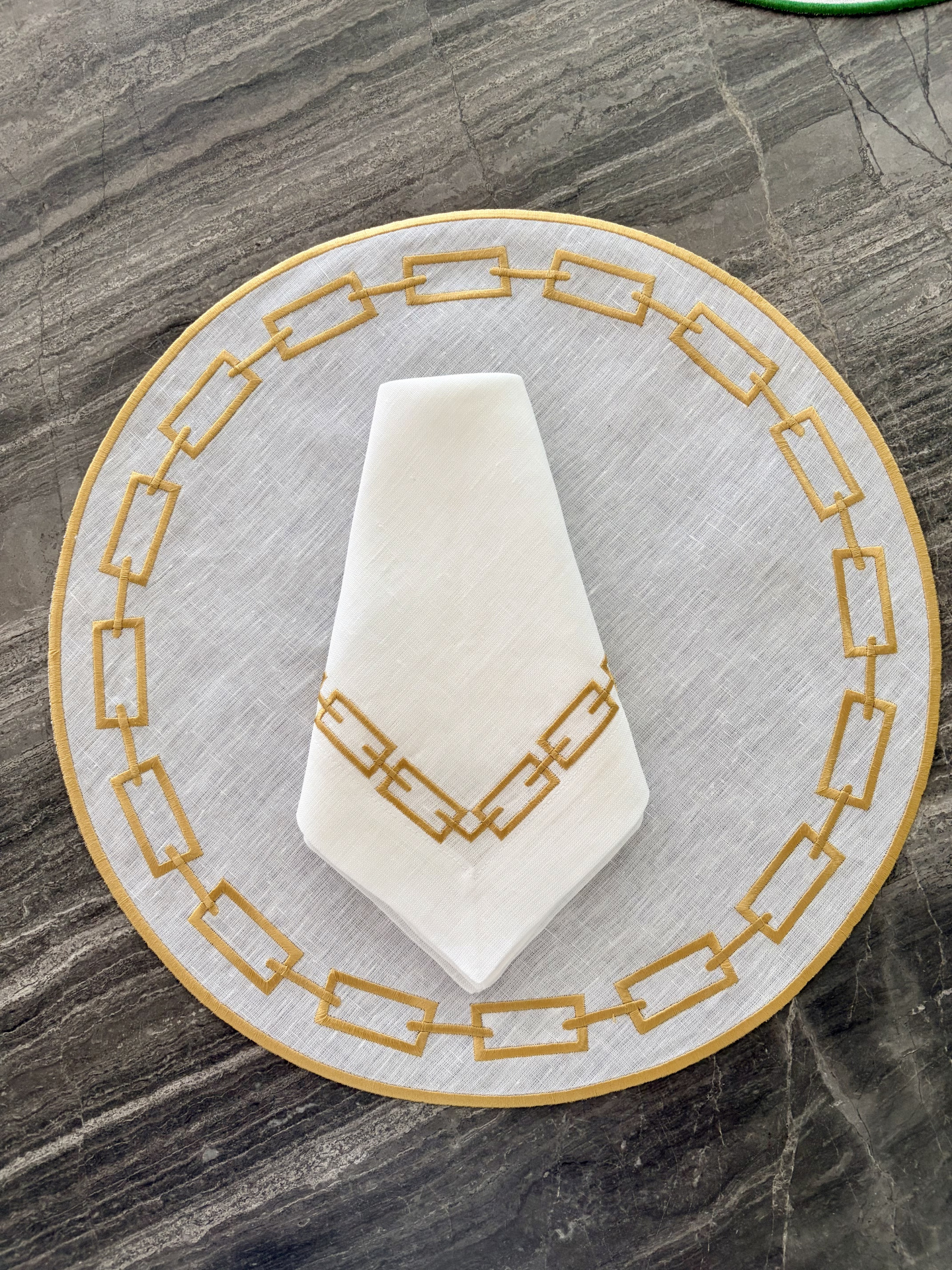 Conjunto de mesa branco com bordado amarelo mostarda sobre superfície de mármore cinza