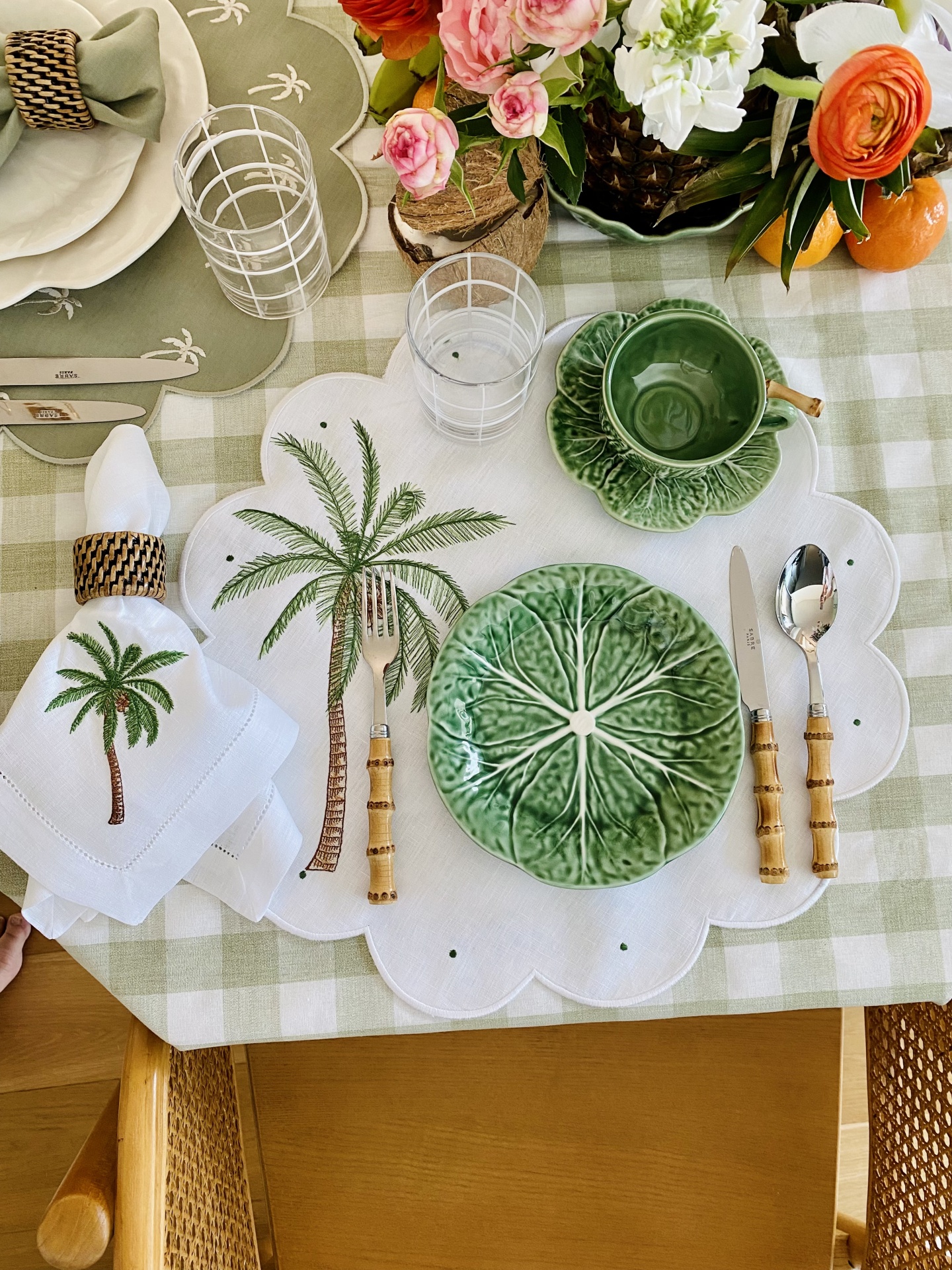 Mesa posta com prato, chávena e talheres com tema de folhas e palmeira, e arranjo floral