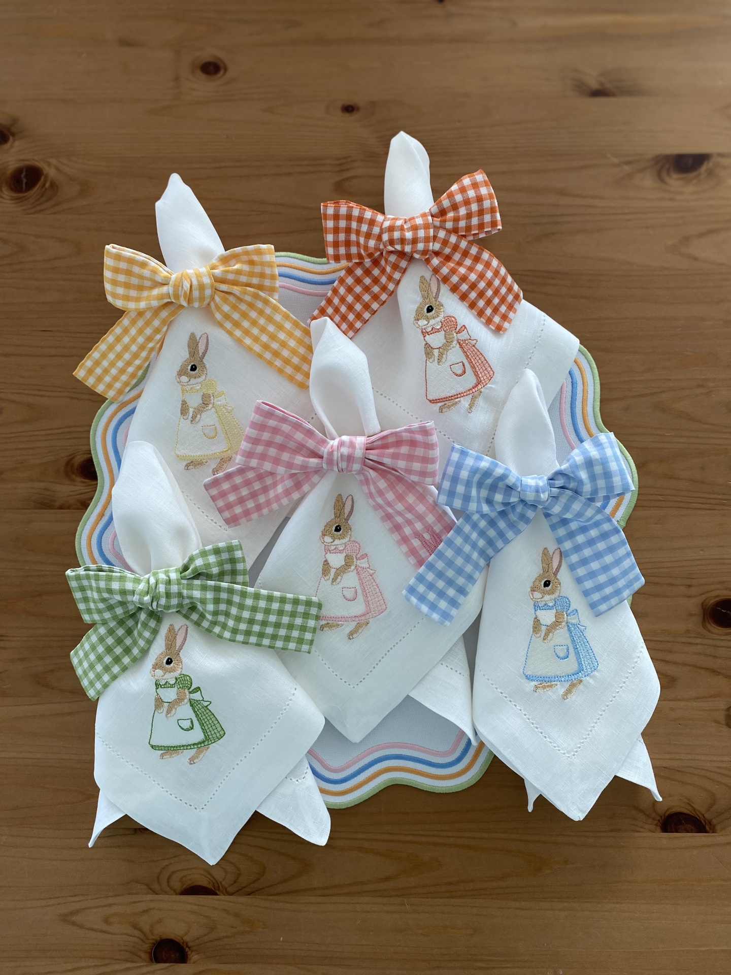 Guardanapos de tecido branco com bordado de coelho e laços xadrez coloridos sobre prato decorativo