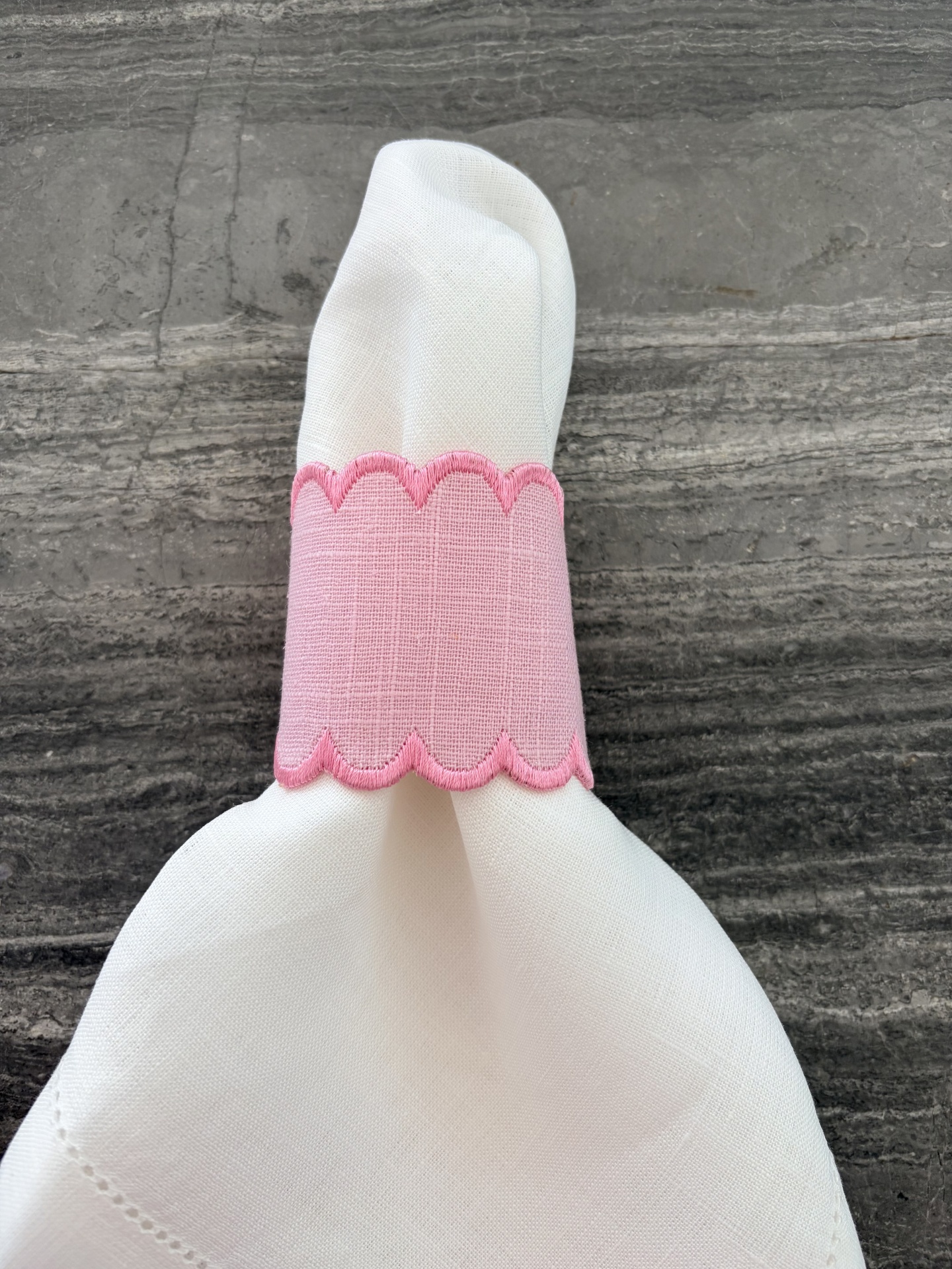 Guardanapo branco com argola rosa bordada sobre superfície cinza