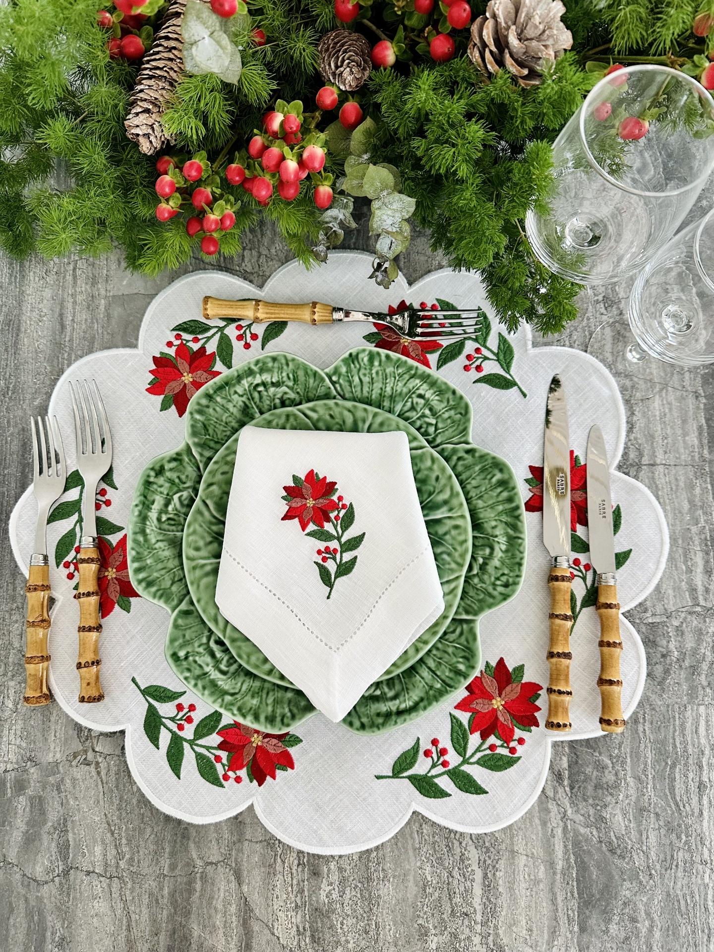 Mesa posta com decoração de flores vermelhas, pratos verdes e talheres com cabos de madeira clara