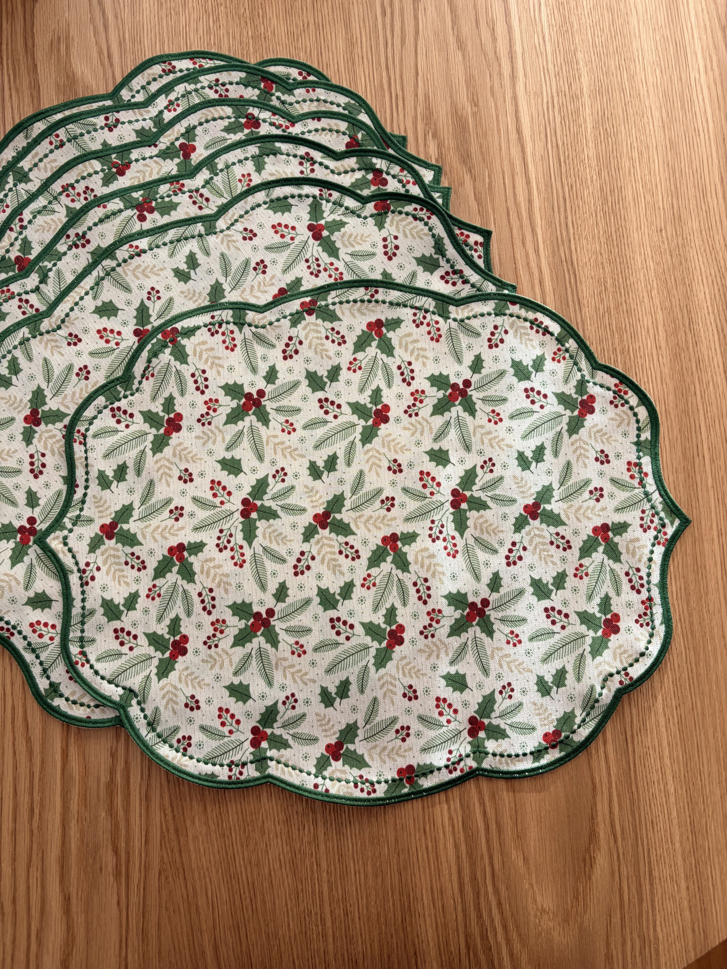 Individuais de mesa com padrão natalício de bagas e folhas, bordas verdes, sobre madeira clara.