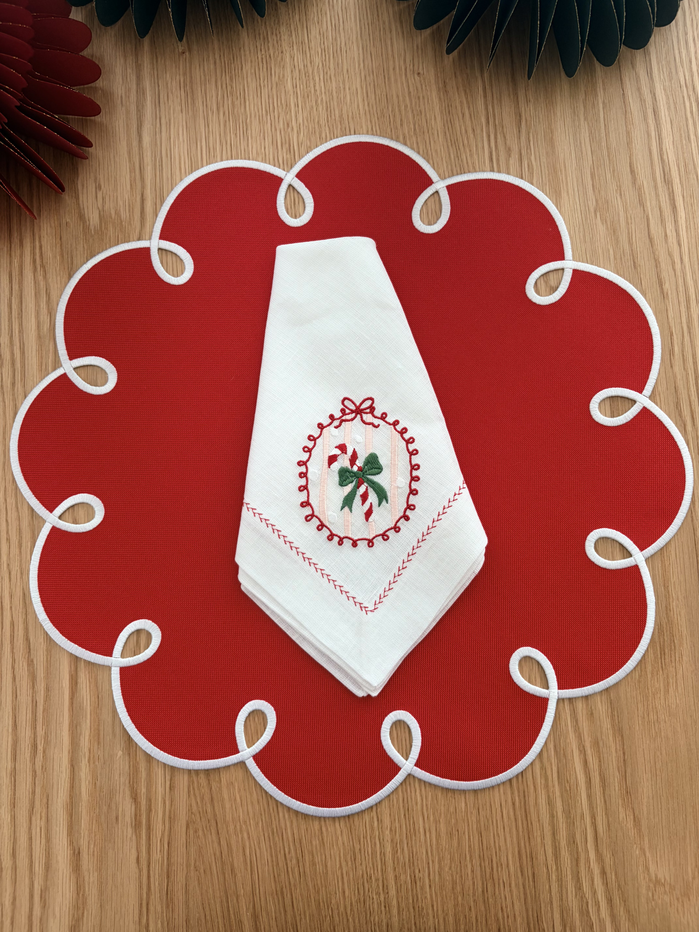 Jogo americano vermelho com bordas brancas e guardanapo branco bordado com motivo natalício