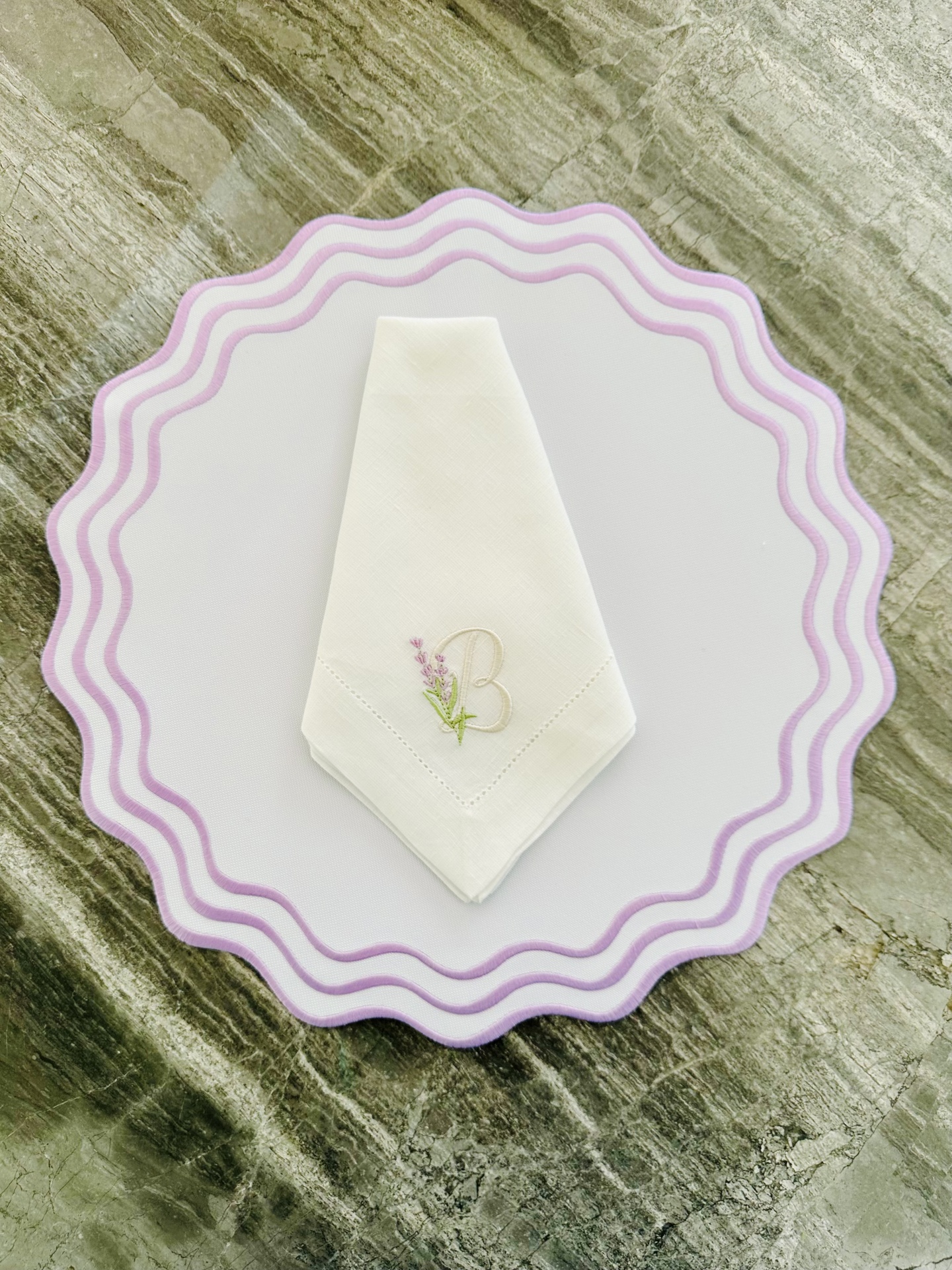 Guardanapo branco bordado com letra B e flor lilás sobre base branca com borda lilás