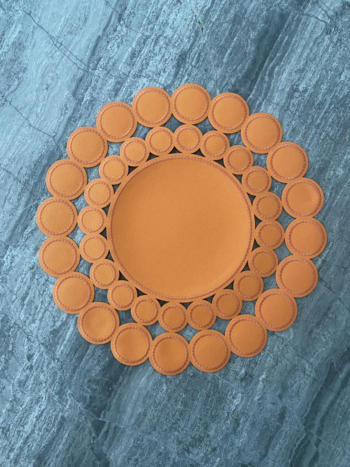 Tapete redondo laranja com círculos concêntricos sobre piso de mármore cinzento