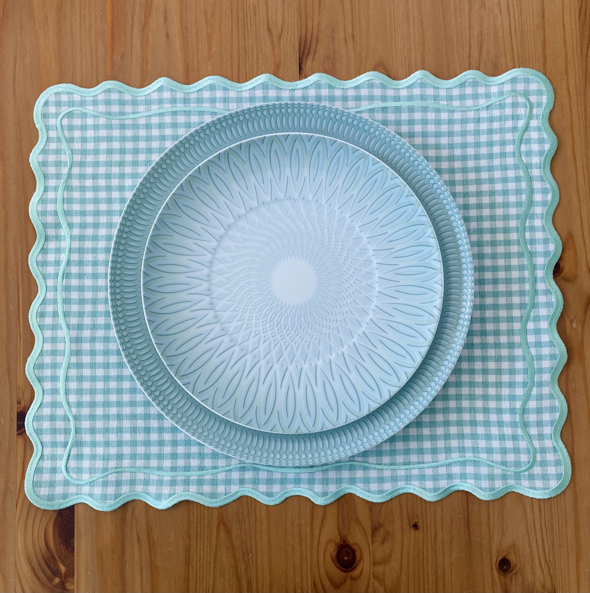 Conjunto de pratos de cerâmica azul claro sobre individual vichy azul e branco em mesa de madeira