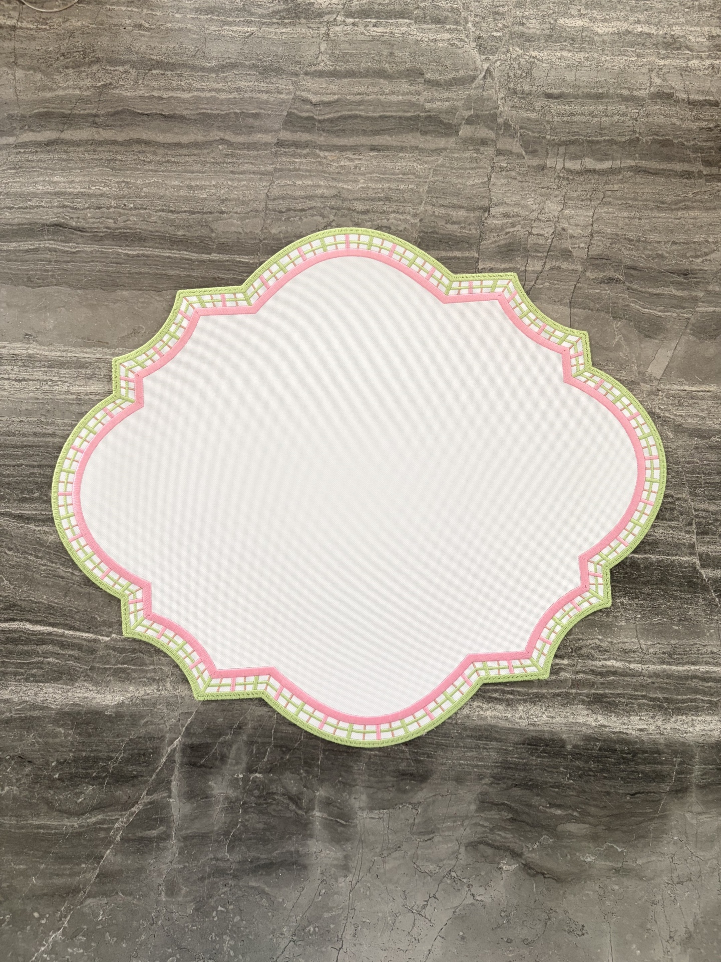 Individual de mesa branco com bordas verde e rosa sobre superfície de mármore cinza